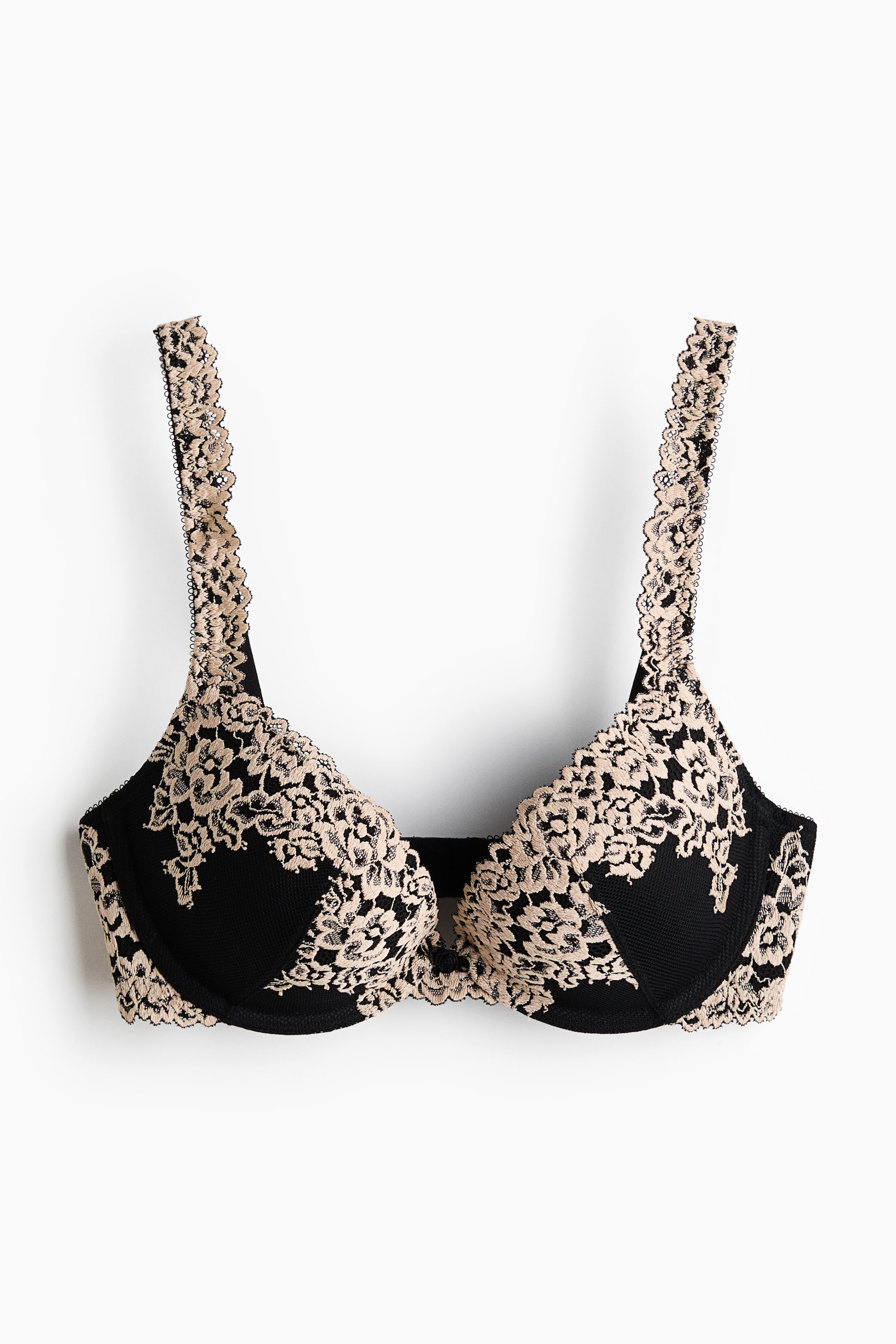 View larger image: The bra is shown from the front, showcasing black underwired cups with a beige floral lace overlay. Scalloped lace edges frame the cups and straps, with a small black bow adorning the center gore.
