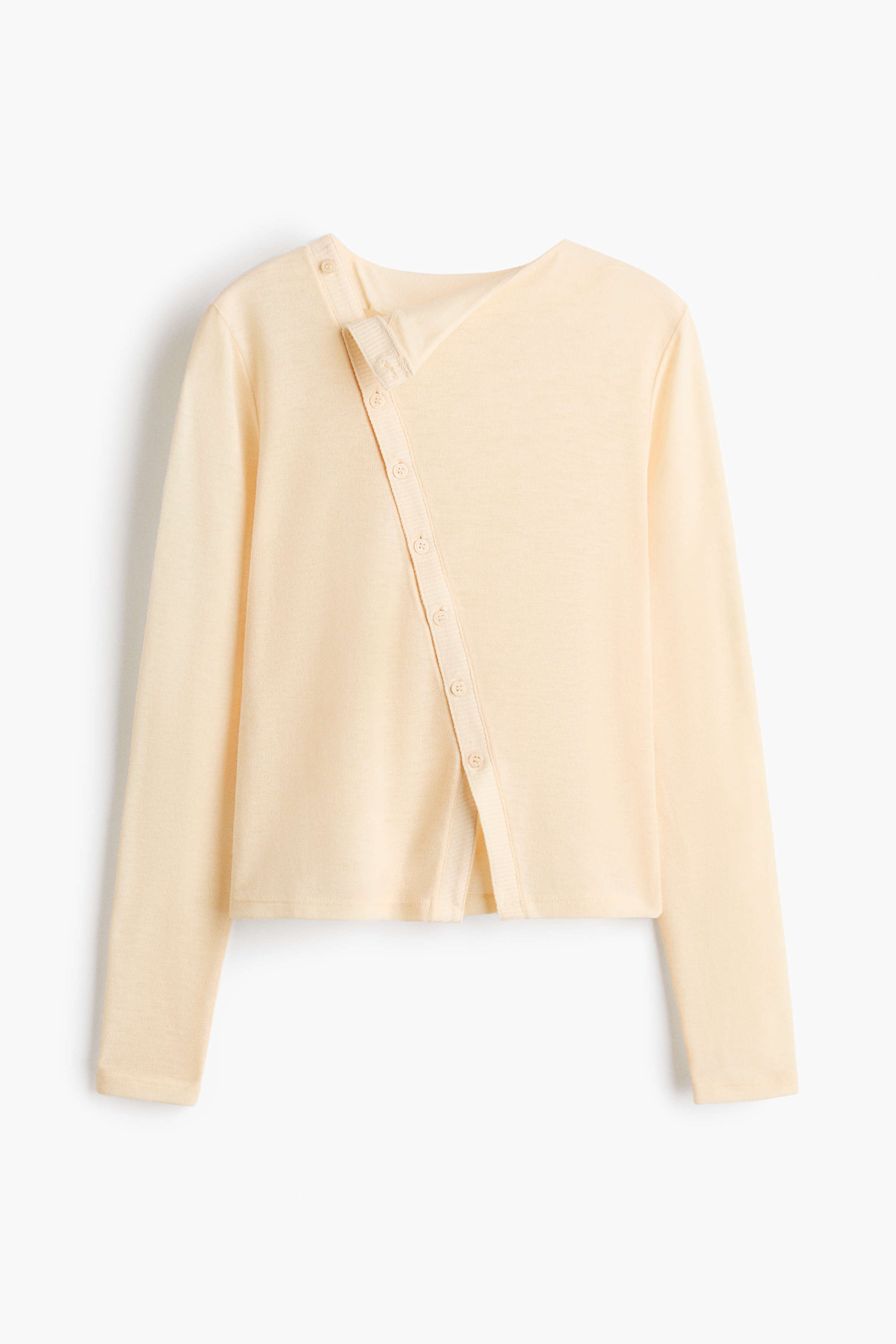The model is wearing a fitted, semi-sheer knit top in cream, featuring a high neckline, long sleeves, and a diagonal button placket down the front. The top is layered over a matching bralette and styled with light-wash denim jeans.