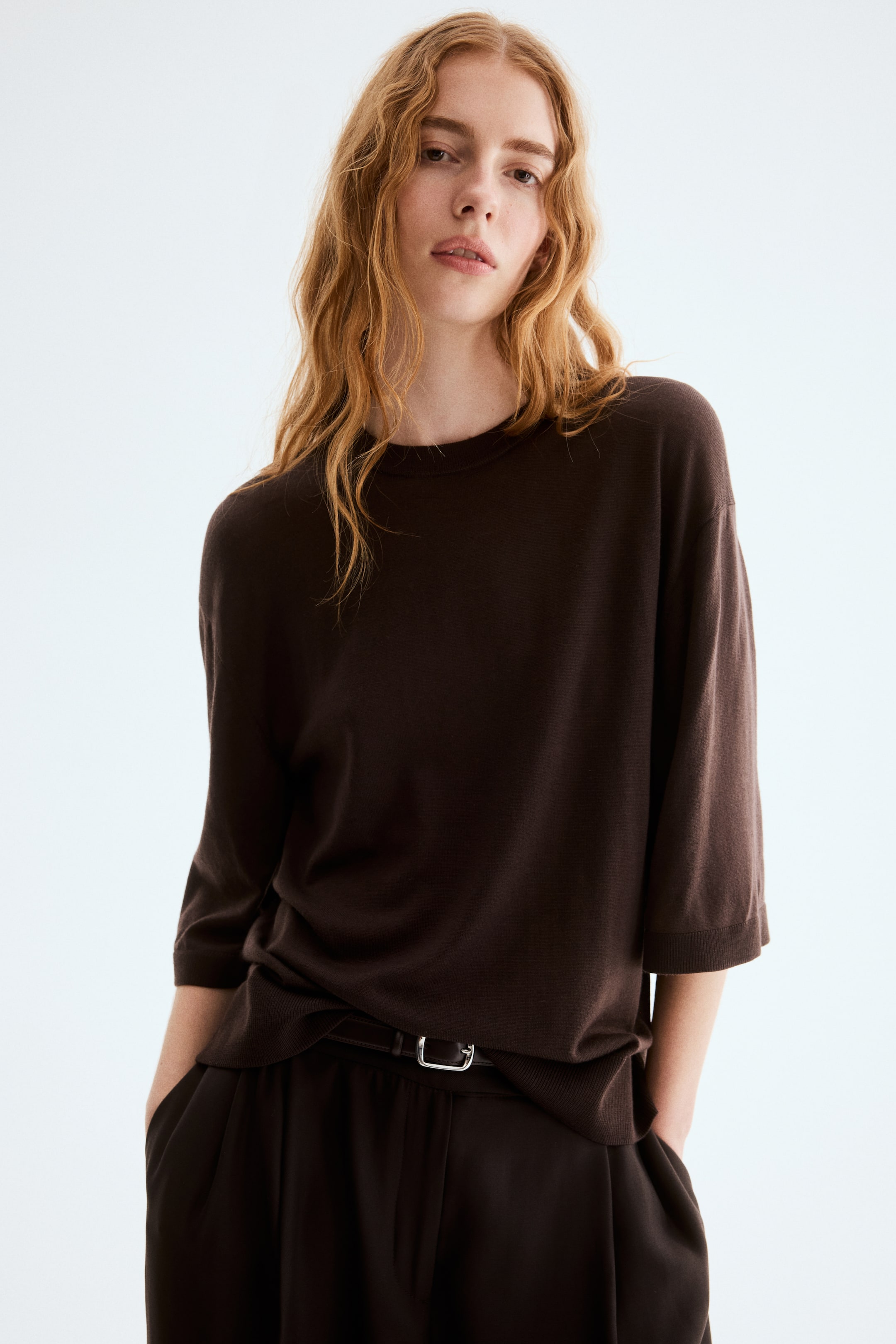 View larger image: A dark brown crew neck top features three-quarter length sleeves with ribbed cuffs and a relaxed fit. The ribbed hem is slightly tucked into pants at the front.
