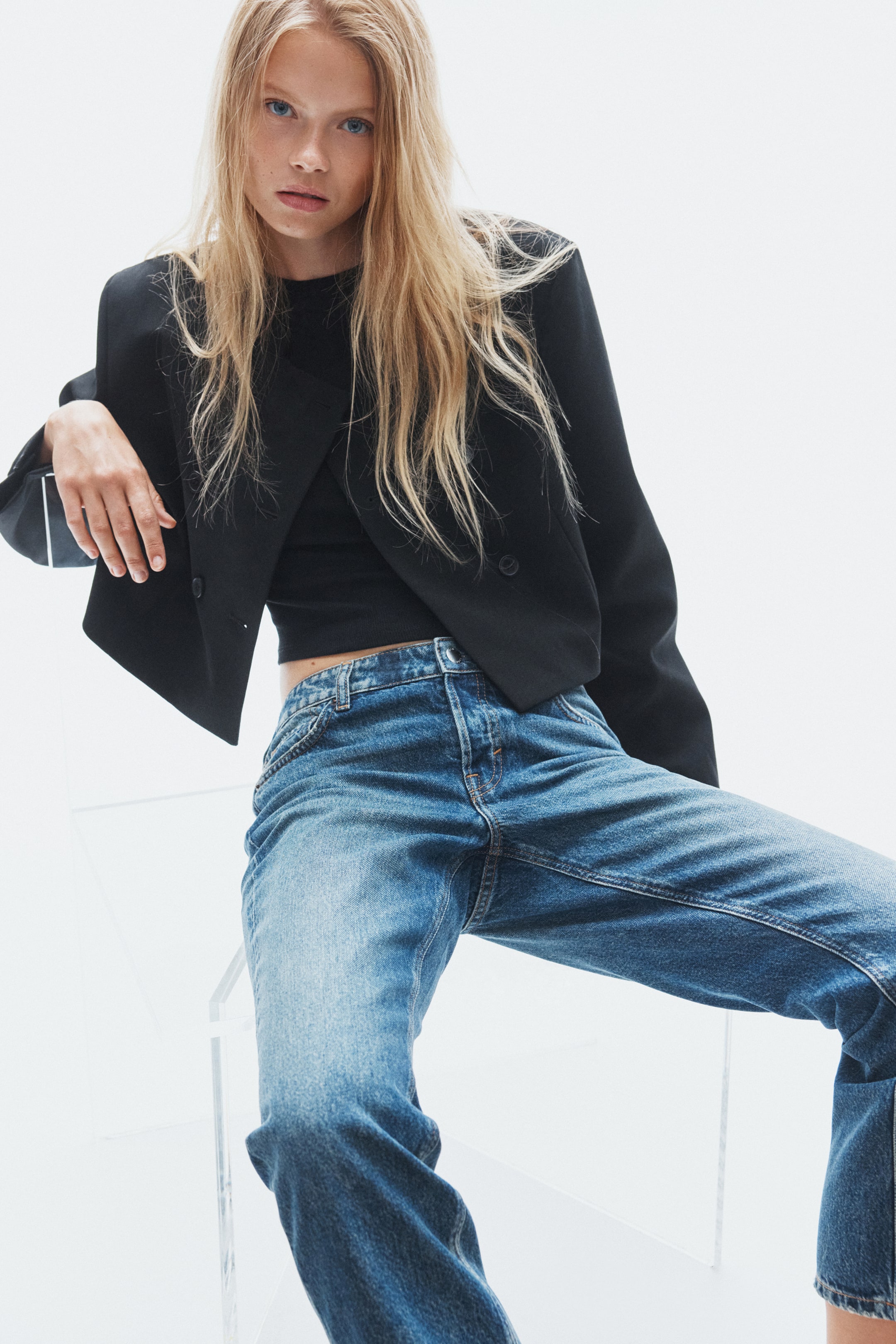 Προβολή μεγαλύτερης εικόνας: Το μοντέλο φορά τζιν σε μεσαία απόχρωση πλύσης, ίσιας γραμμής, σε μπλε χρώμα, συνδυασμένα με ένα κοντό μαύρο blazer φορεμένο πάνω από ένα μαύρο top. Τα τζιν διαθέτουν ξεθωριασμένο φινίρισμα και άνετη εφαρμογή, αναδεικνύοντας τον casual σχεδιασμό τους.