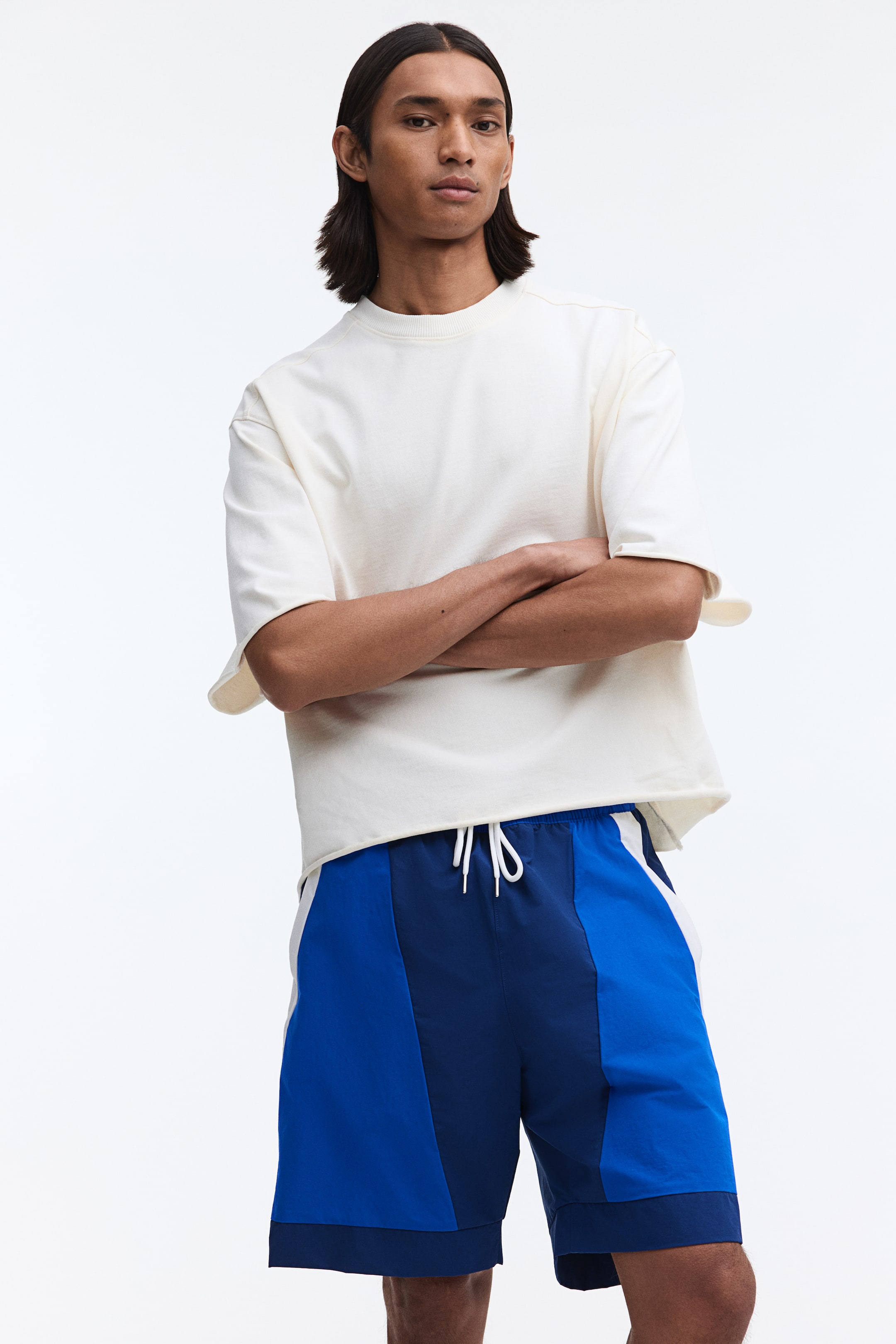 View larger image: These shorts showcase a colour-blocked design with panels of royal blue, navy blue, and a vertical white stripe. They feature an elasticated waistband with white drawstrings and fall to approximately knee length.