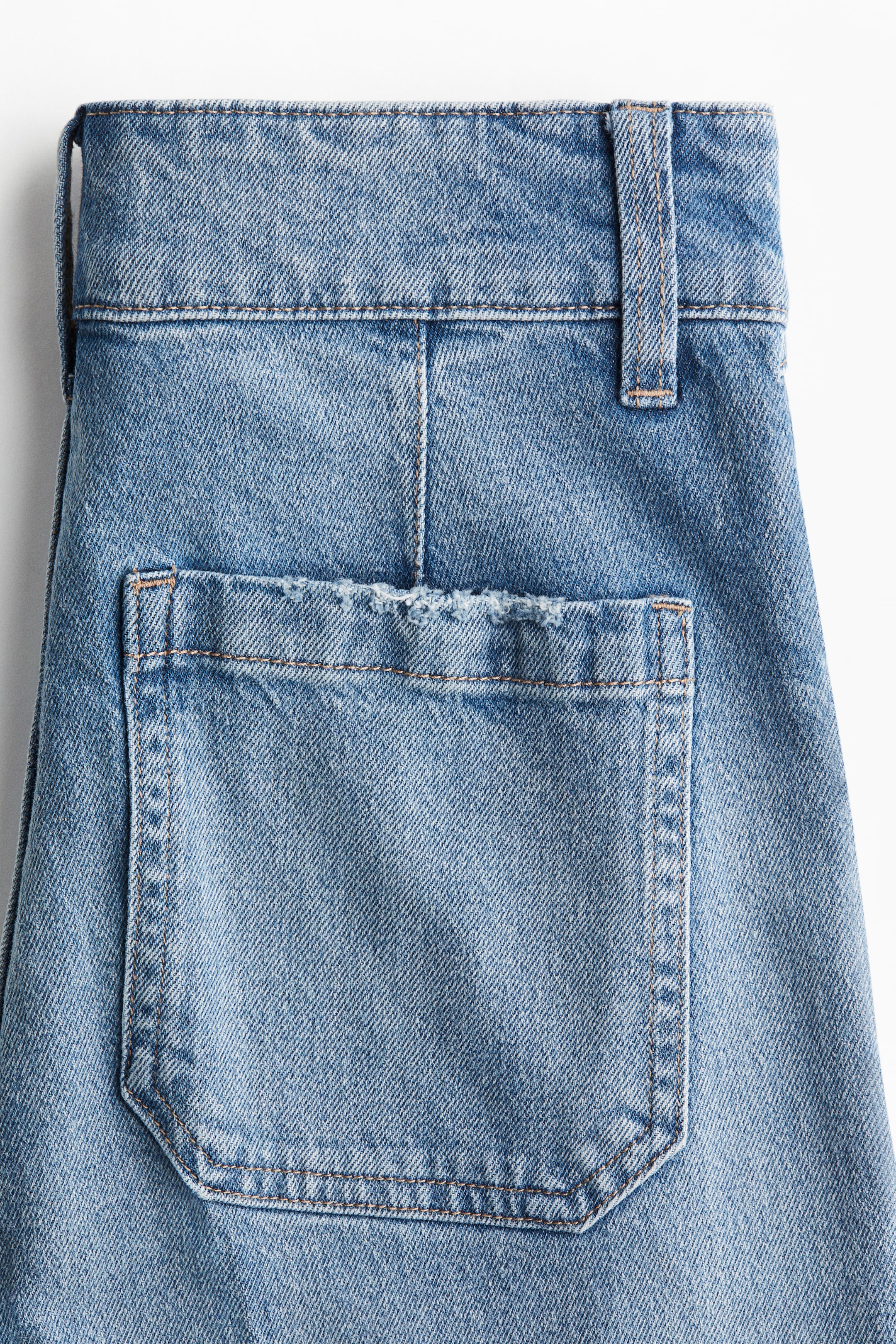 Visualizza immagine più grande: Jeans in denim di cotone azzurro mostrano una cintura larga con passanti per cintura e una grande tasca posteriore a toppa sulla destra. Cuciture a contrasto definiscono la tasca, la cintura e una cucitura centrale verticale sul retro, con il bordo superiore della tasca che appare leggermente consumato.