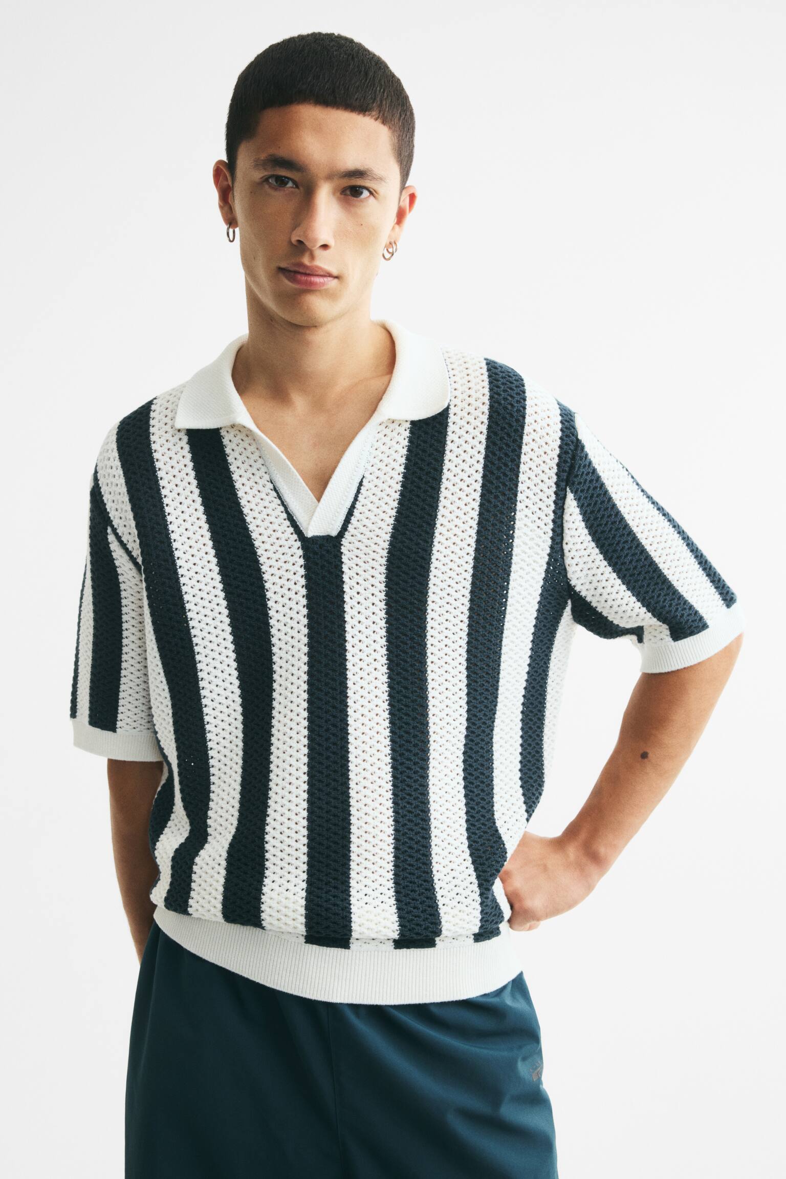 A short-sleeved knitted polo shirt showcasing an open-knit texture with vertical dark green and off-white stripes. It features a pointed collar, a V-neck opening, and ribbed cuffs and hem. - 1