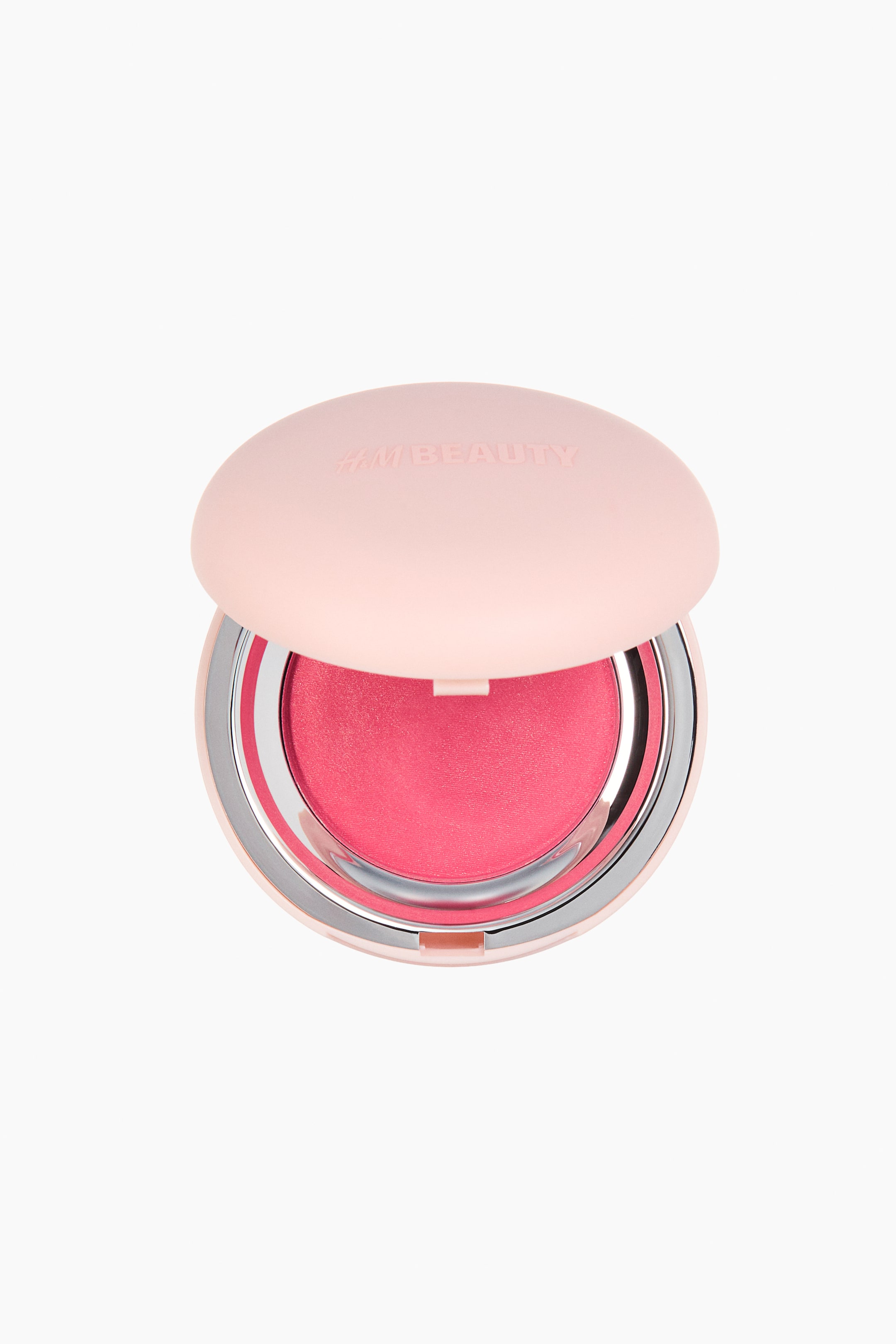View larger image: A round cream-to-powder blush compact shown from the front, its pale pink lid slightly open to reveal "H&M BEAUTY" embossed on the surface. Inside, a bright fuchsia blush pan is visible, surrounded by a silver-toned rim.