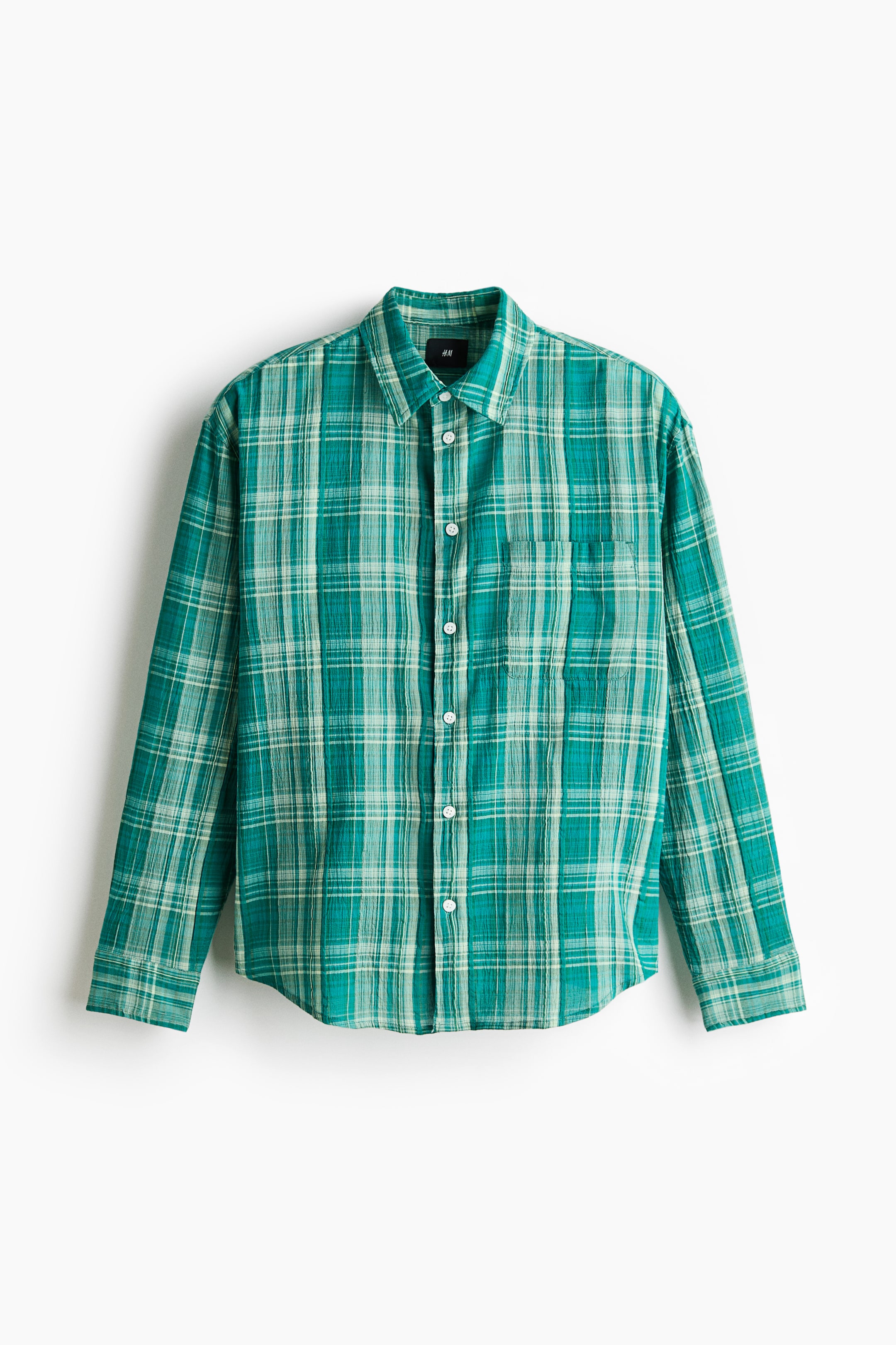 View larger image: A green and off-white plaid shirt is showcasing a front view, highlighting a crinkled texture. It is crafted with a pointed collar, a complete button-front closure with white buttons, long sleeves with single-button cuffs, and a single patch pocket on the left chest.