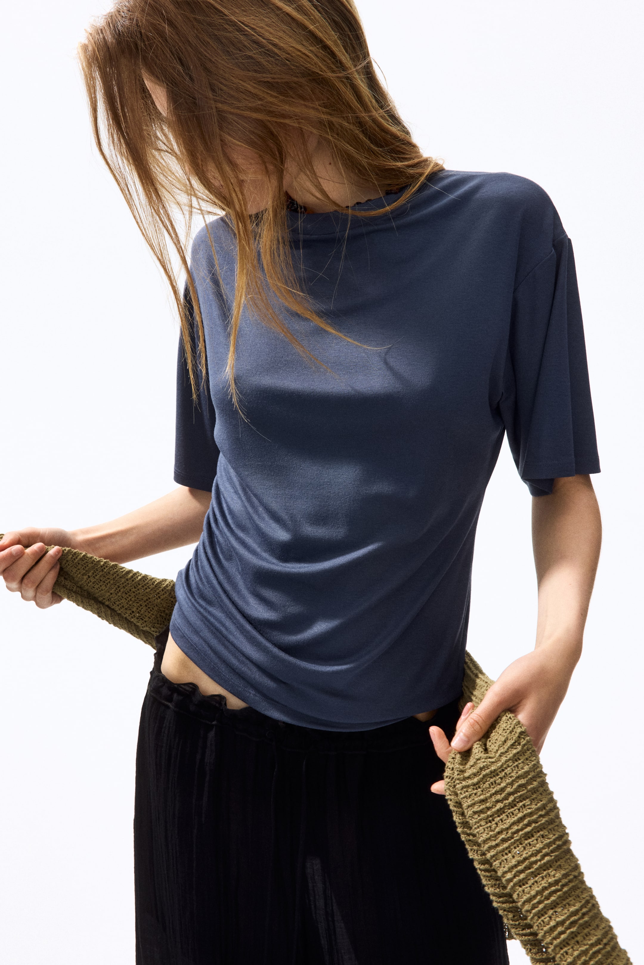 View larger image: The dark blue t-shirt, shown from the front, features a crew neck with a subtly wavy edge and short, relaxed-fit sleeves. It fits snugly to the torso, showcasing visible ruching on the lower left side.