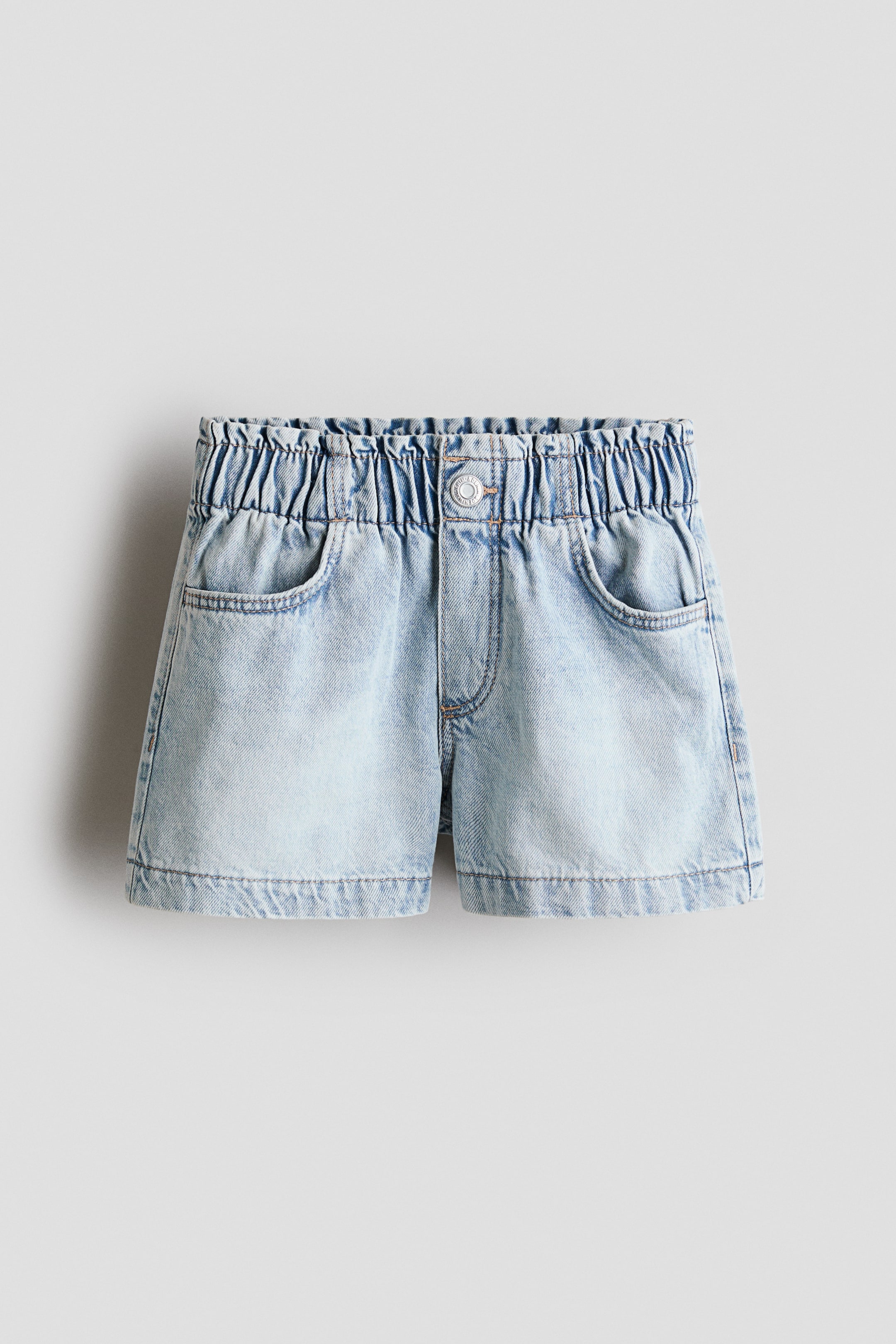 Agrandir l'image: Shorts coupe ample en denim de coton délavé, présentés de face. Ils sont dotés d'une taille élastiquée paper bag, d'une fausse braguette avec press-stud et de poches diagonales à l'avant.