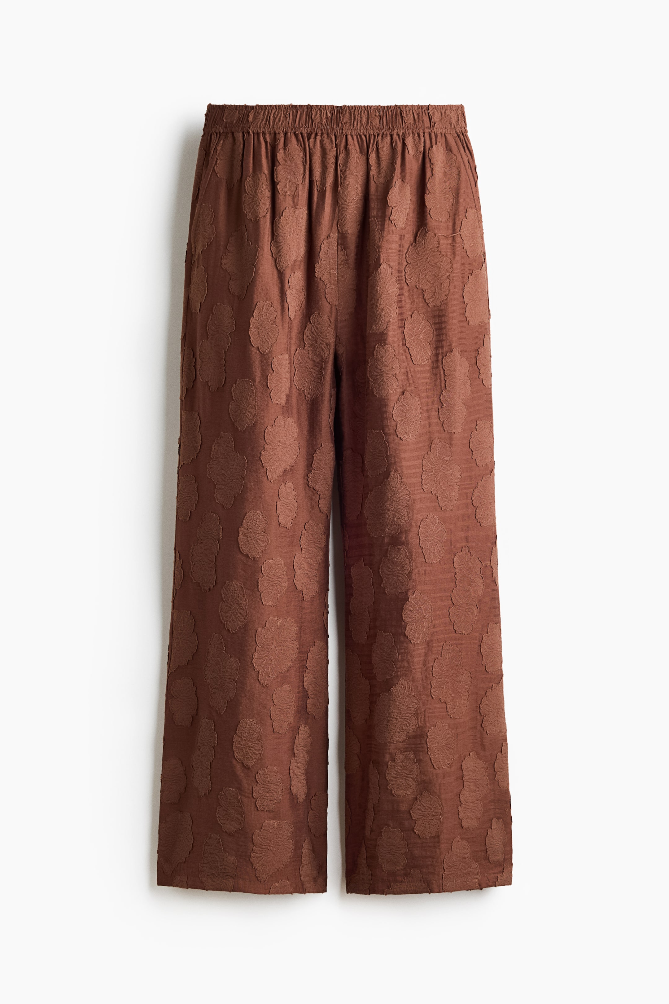 View larger image: The brown trousers feature an elasticated waistband and a wide-leg, cropped silhouette, with the fabric showcasing an all-over raised textured pattern of abstract shapes.