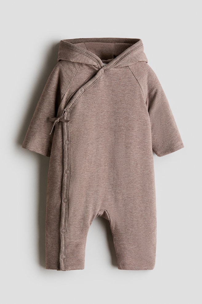 Un pramsuit marrone melange H&M Adorables si presenta con maniche raglan, un cappuccio foderato e una parte anteriore incrociata fissata con lacci e bottoni a pressione su un lato. Altri bottoni a pressione si estendono lungo una gamba, mentre le maniche e le gambe hanno polsini semplici. - 1