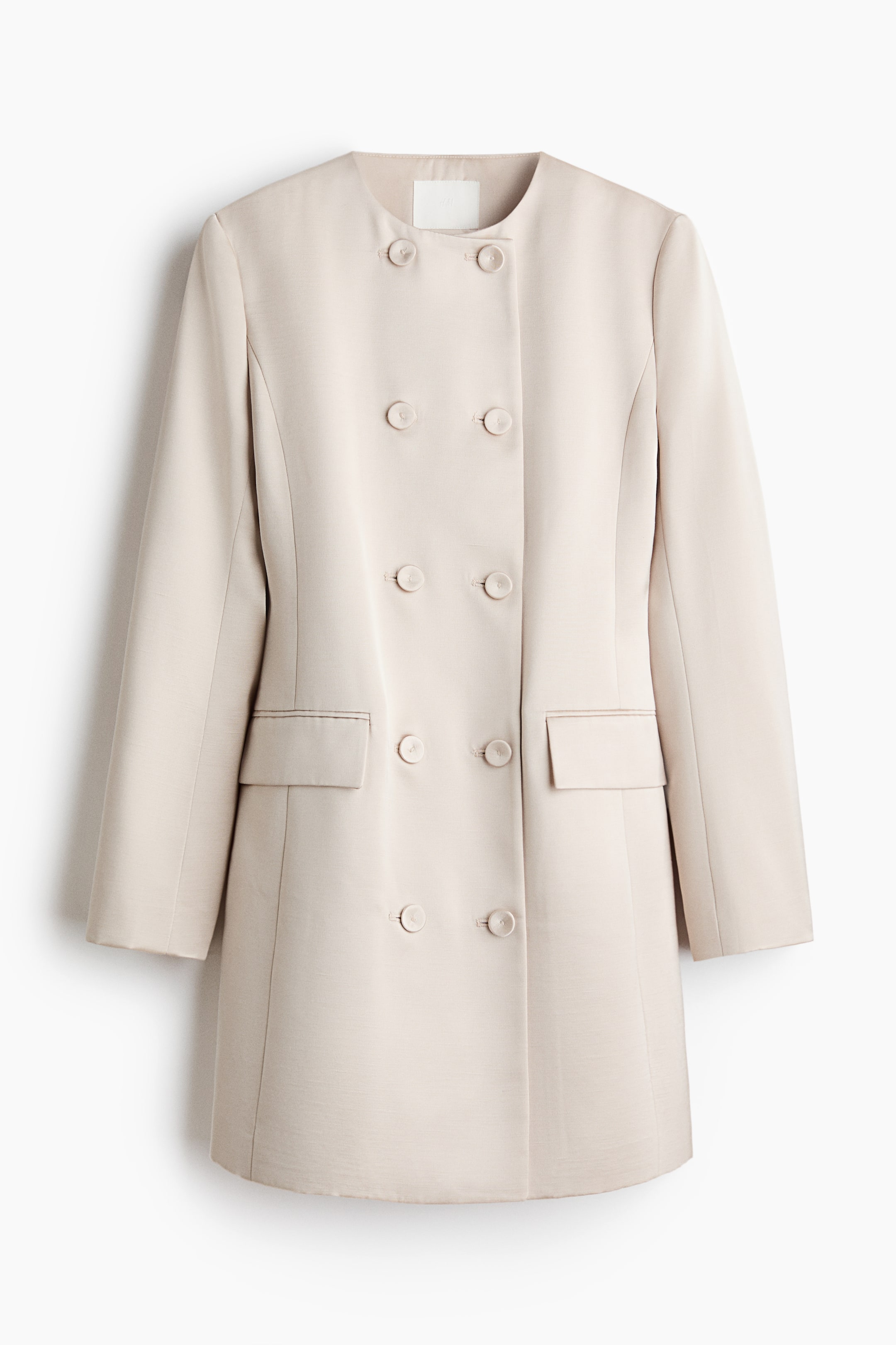 View larger image: A short, light beige blazer dress is presented from the FRONT, featuring a round neckline and a double-breasted closure with six buttons. It is also displaying structured shoulders and two jetted pockets with flaps on the lower front.
