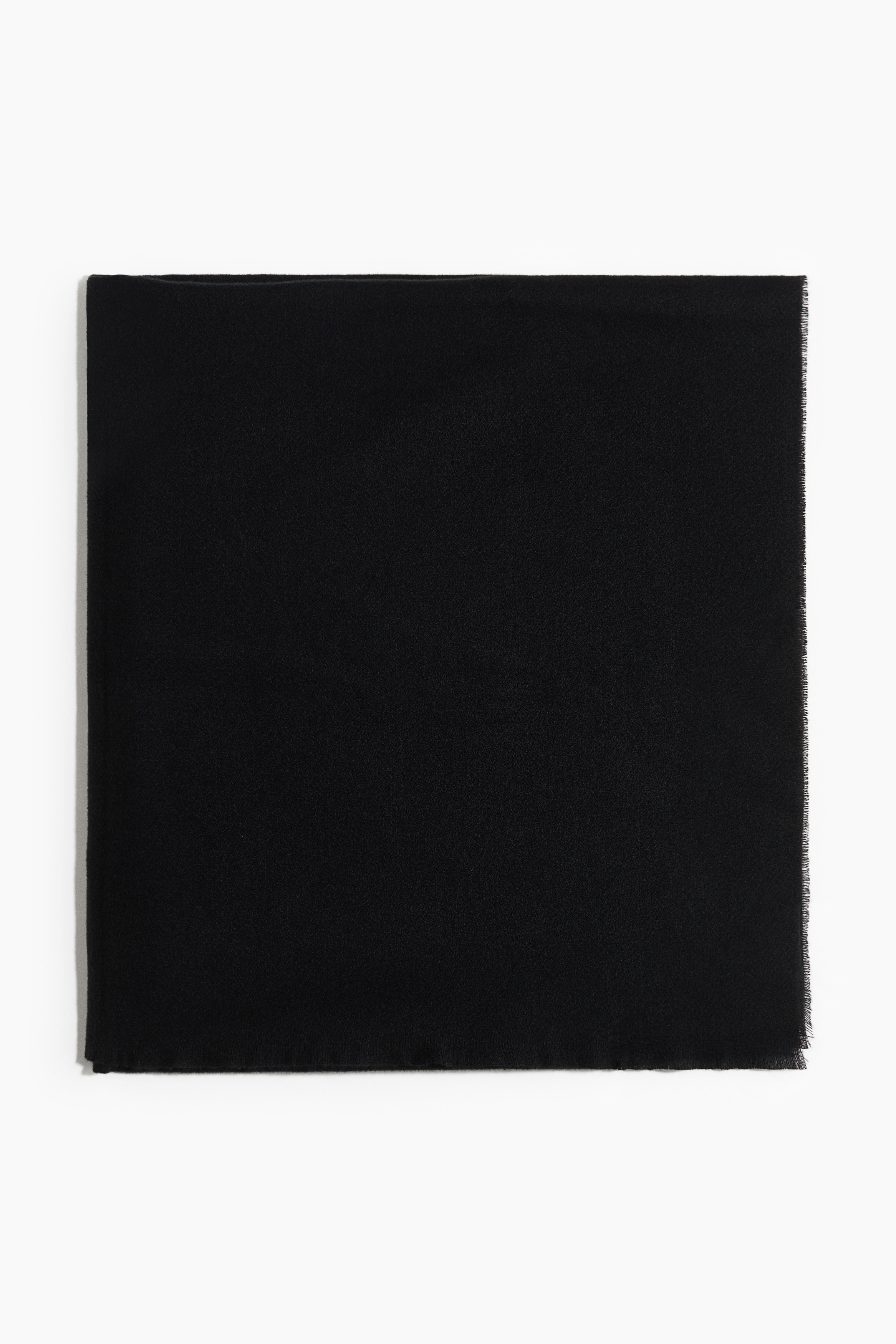 A black blanket scarf in a soft weave with frayed edges is being worn by the model, wrapped around the neck with its long ends draped down the front of a dark leather coat.