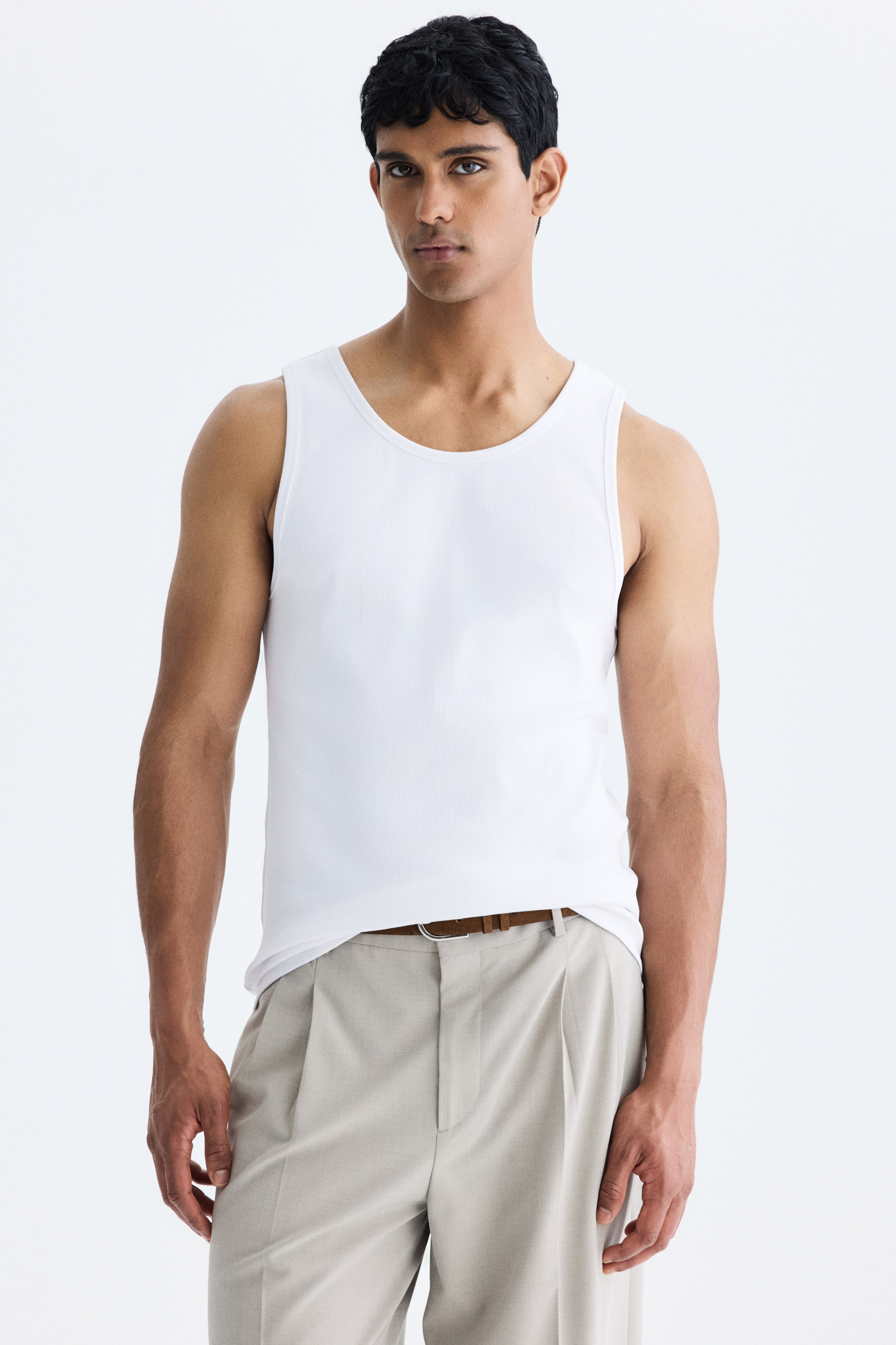 View larger image: Model mengenakan baju dalam berpotongan slim-fit diperbuat daripada fabrik kapas berjalur. Baju dalam berwarna putih ini mempunyai leher bulat dan dimasukkan ke dalam seluar panjang berlipat berwarna cerah, yang diikat dengan tali pinggang coklat.