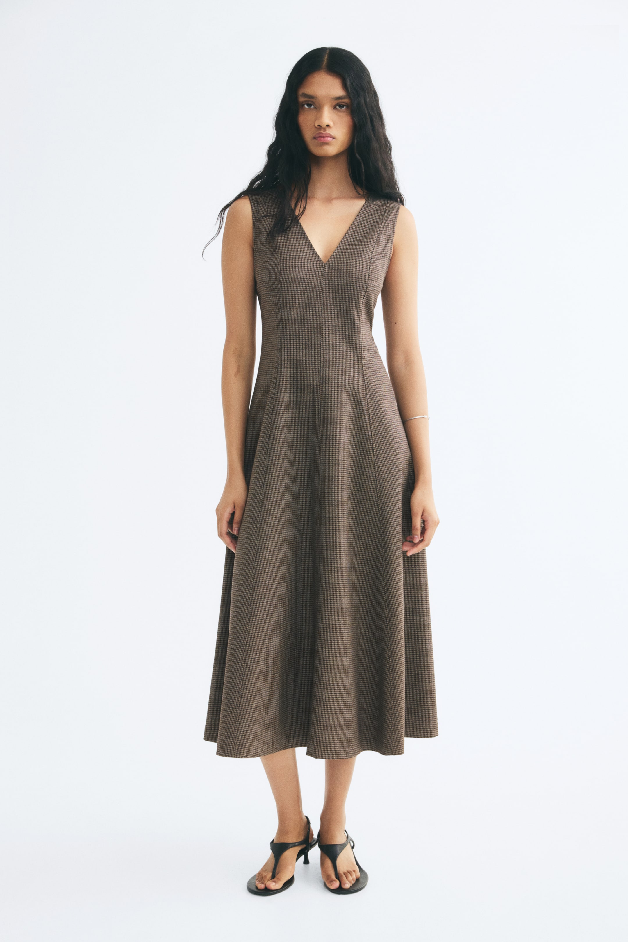 View larger image: A calf-length, sleeveless dress in a brown patterned woven fabric is being worn by the model. The dress features a V-neckline, a fitted bodice with visible vertical seams, and a flared skirt.