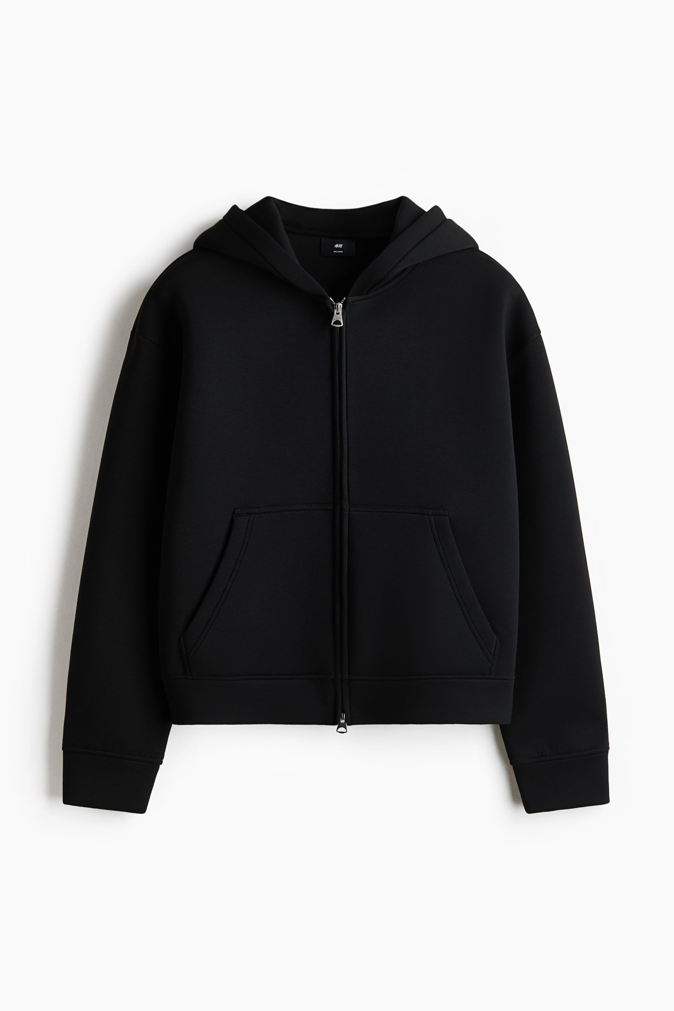 View larger image: A black zip-up hoodie is shown from the front, featuring a boxy, relaxed fit with dropped shoulders. It's crafted from smooth scuba fabric and includes a lined hood, a front zipper, and open front pockets.
