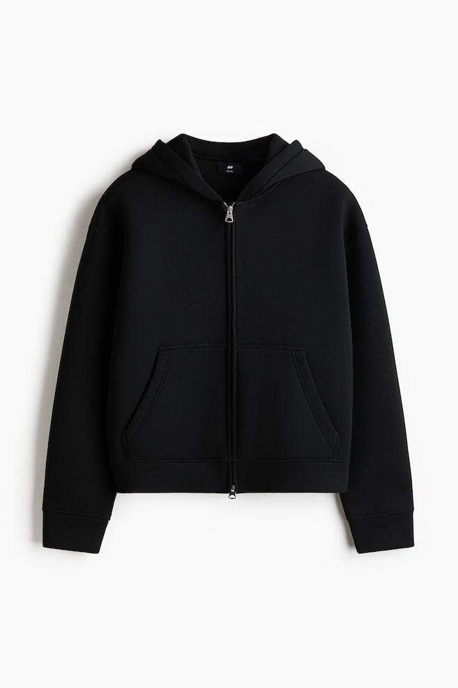 A black zip-through hoodie is showcased at the front, featuring a boxy, relaxed fit with dropped shoulders. Made from smooth scuba fabric, it includes a lined hood, a front zipper, and open front pockets. - 1