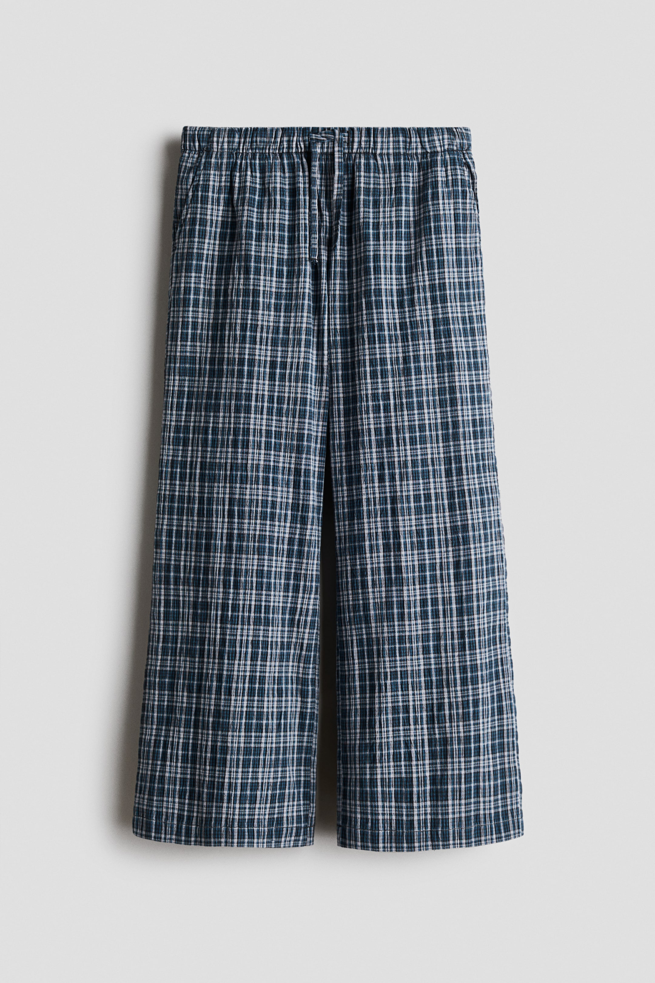 View larger image: The trousers display a dark blue and green checked pattern with white intersecting lines. They feature an elasticated waistband with a visible drawstring and wide, straight-cut legs, presented in a front-facing view.