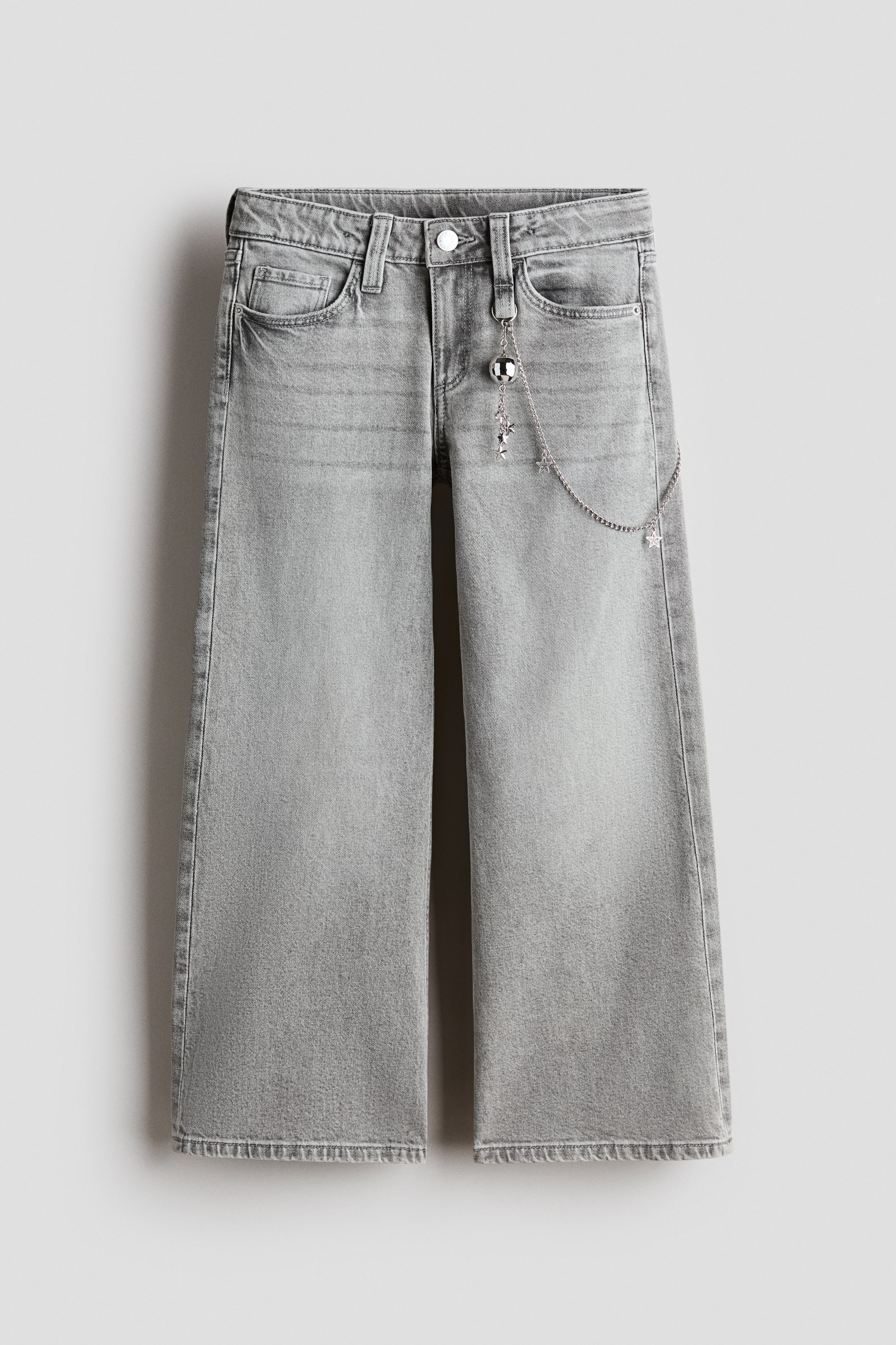 View larger image: FRONT view of gray-washed denim 5-pocket jeans featuring a baggy fit through the hip and thigh with flared legs. The low-rise jeans display a zip fly with a button closure and a decorative silver-toned chain with sphere and star charms attached to a front belt loop.