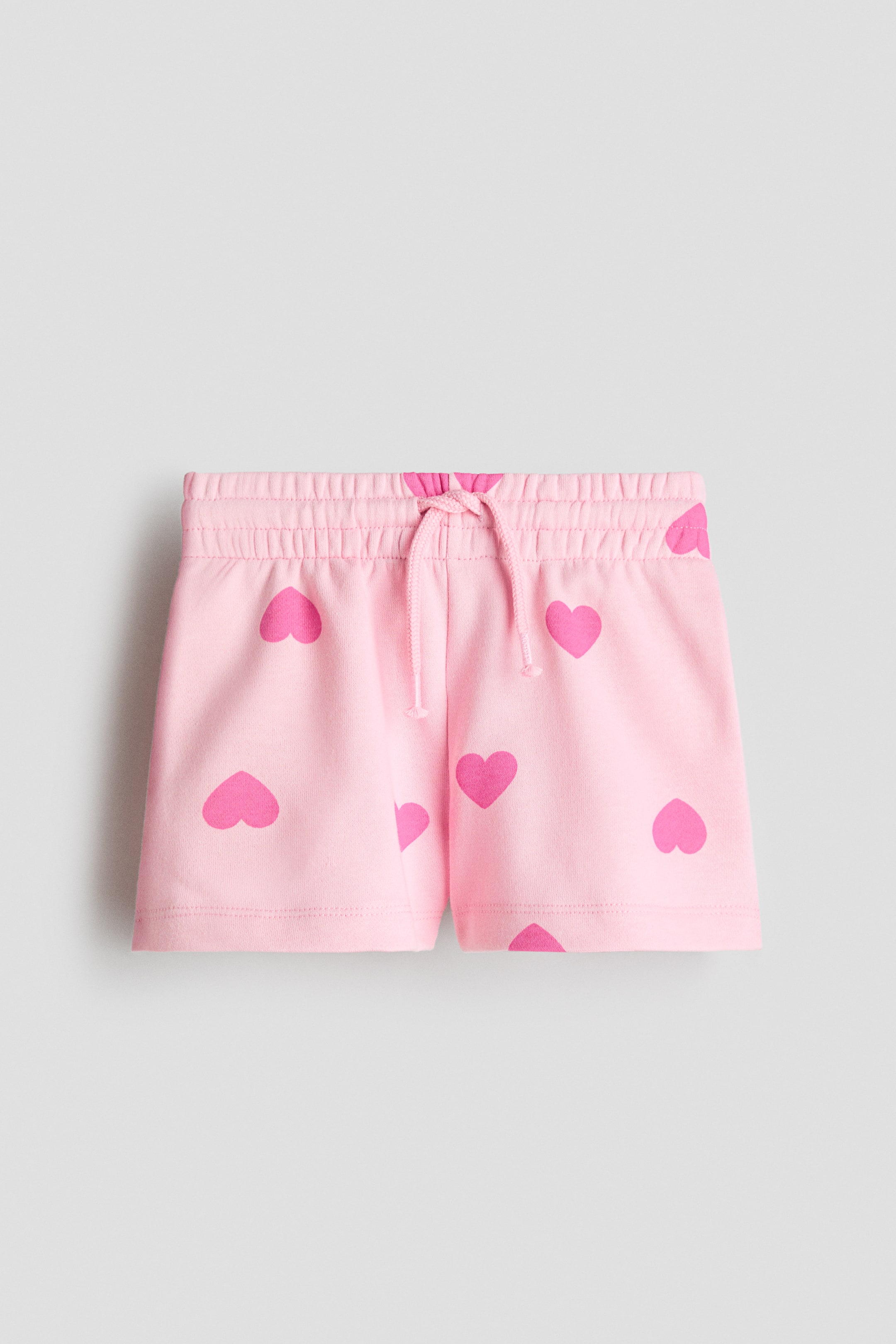 View larger image: Front-facing pink shorts feature an elasticated, ruched waistband with a pink drawstring tie. Hot pink heart graphics are scattered across the fabric.