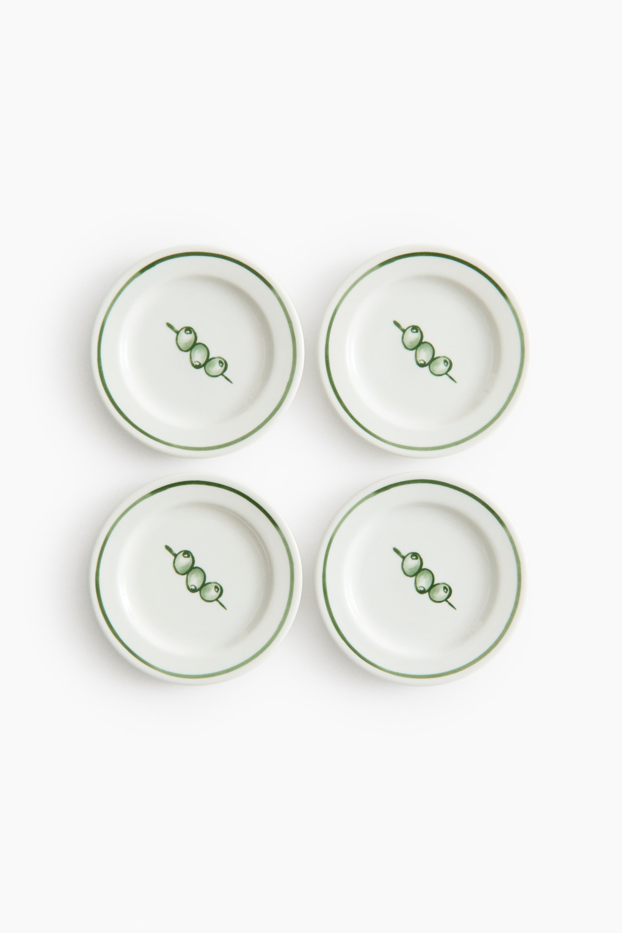 拡大画像を表示: 4枚セットの小さな磁器プレートは、クラシックな緑のペイントリムと楽しい配置プリントが特徴です。各白いプレートの中央には、スティックに3つの緑のオリーブ形が描かれています。