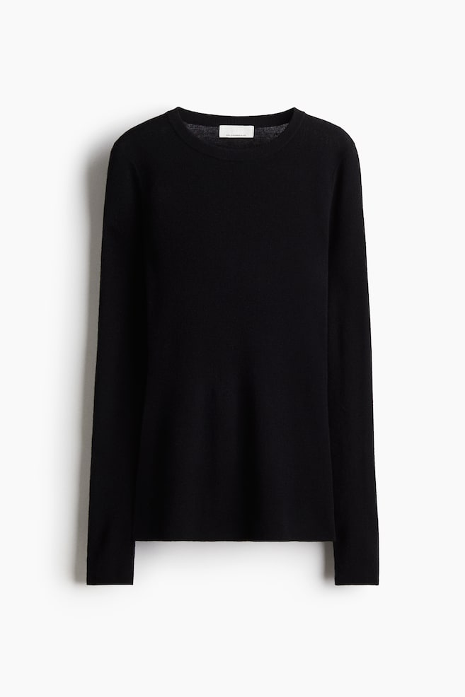 A black knit top is presented facing front, displaying a fine, smooth knit texture. It is designed with a round, rib-trimmed neckline, long sleeves, and a straight hem. - 1