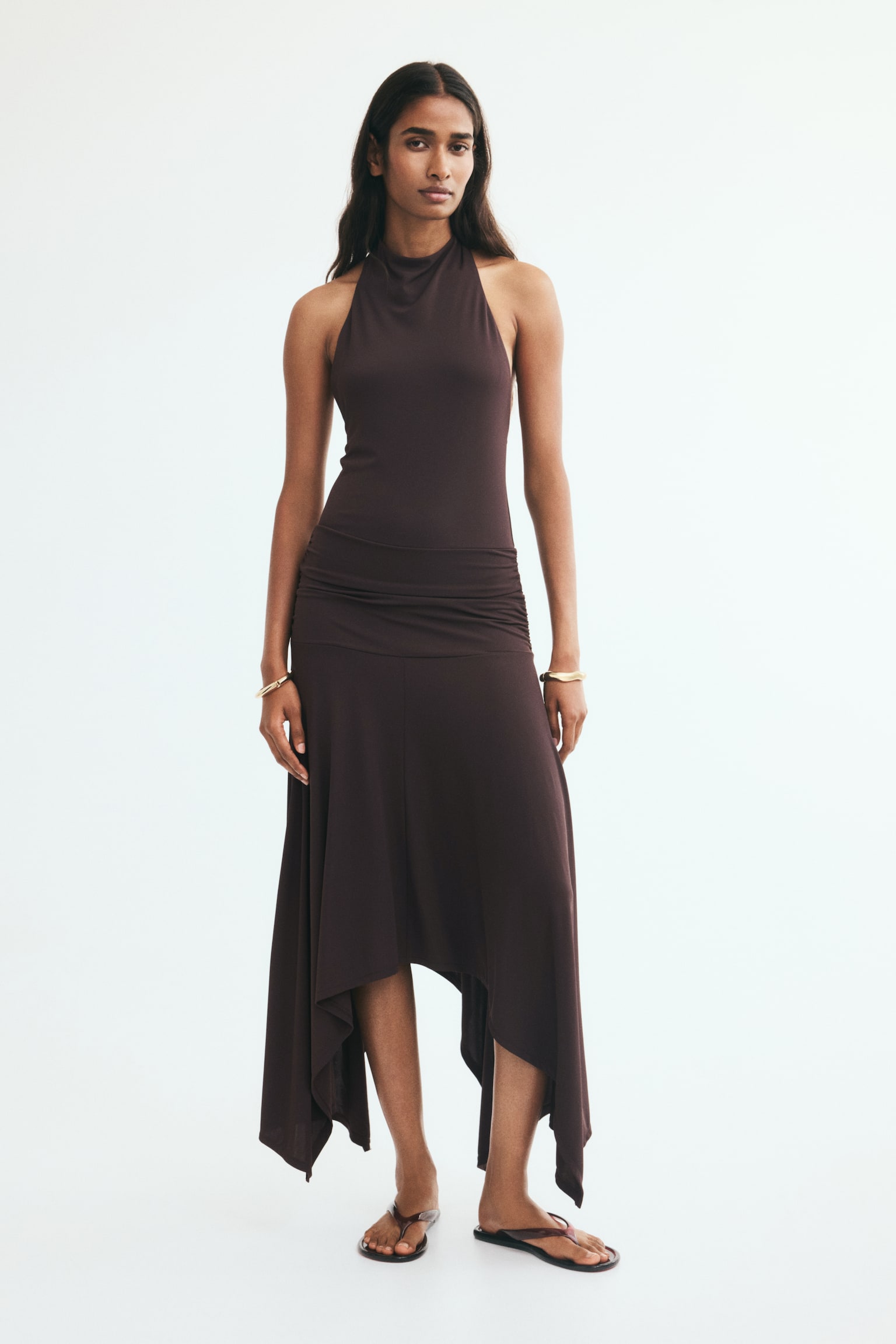 A dark brown halterneck dress featuring a draped neckline, a ruched mid-section, and an asymmetrical handkerchief hem. - 1