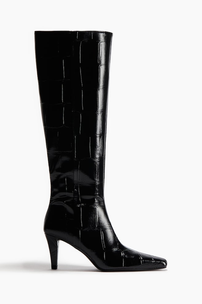 Une seule botte noire est debout, avec une tige haute et une texture brillante en relief crocodile. Elle présente un bout carré et un talon bas et élancé. - 1