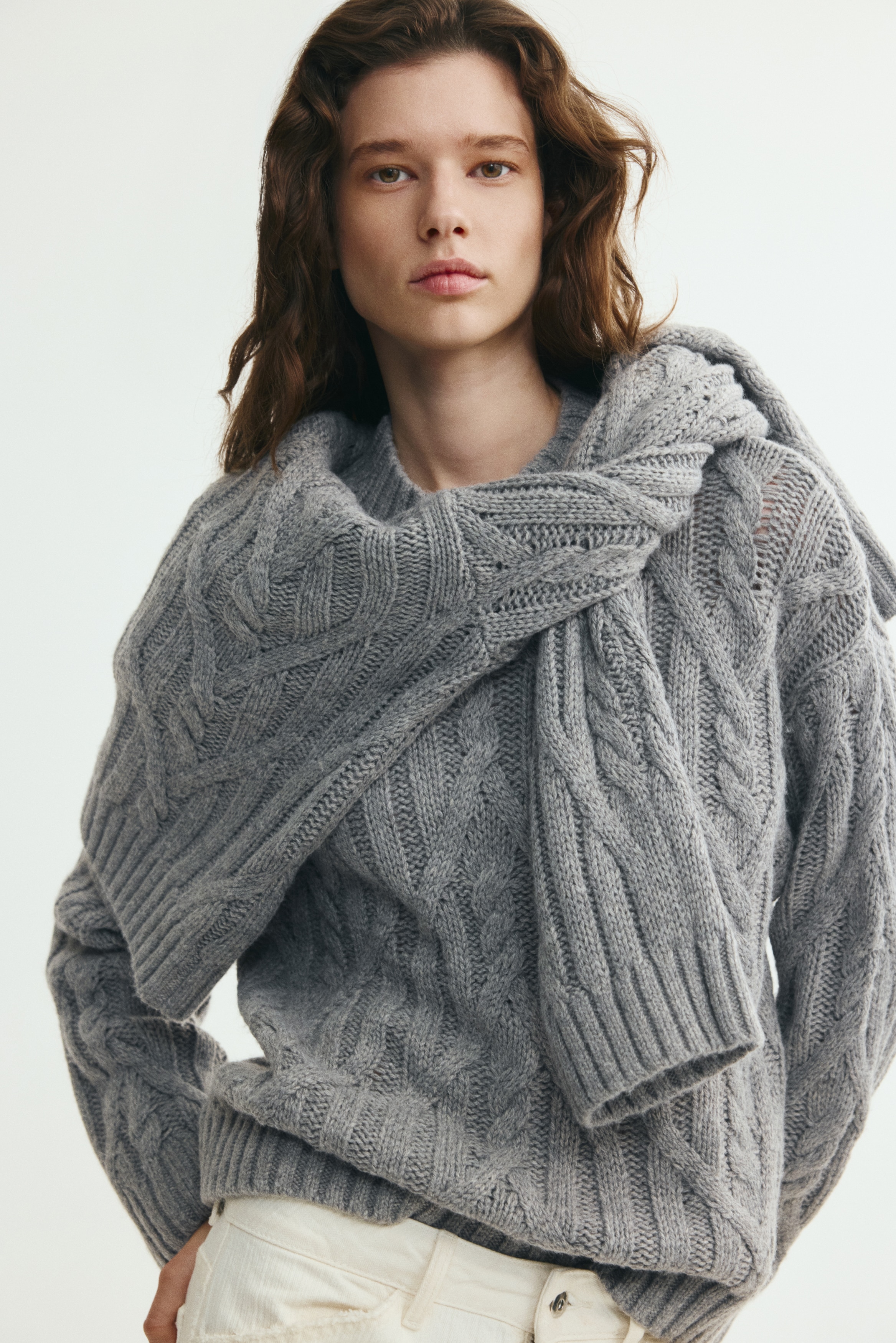 A grey cable-knit jumper is facing front, displaying an intricate all-over diamond cable-knit pattern. The jumper features a ribbed mock neck, relaxed-fit long sleeves with ribbed cuffs, and a ribbed hem.