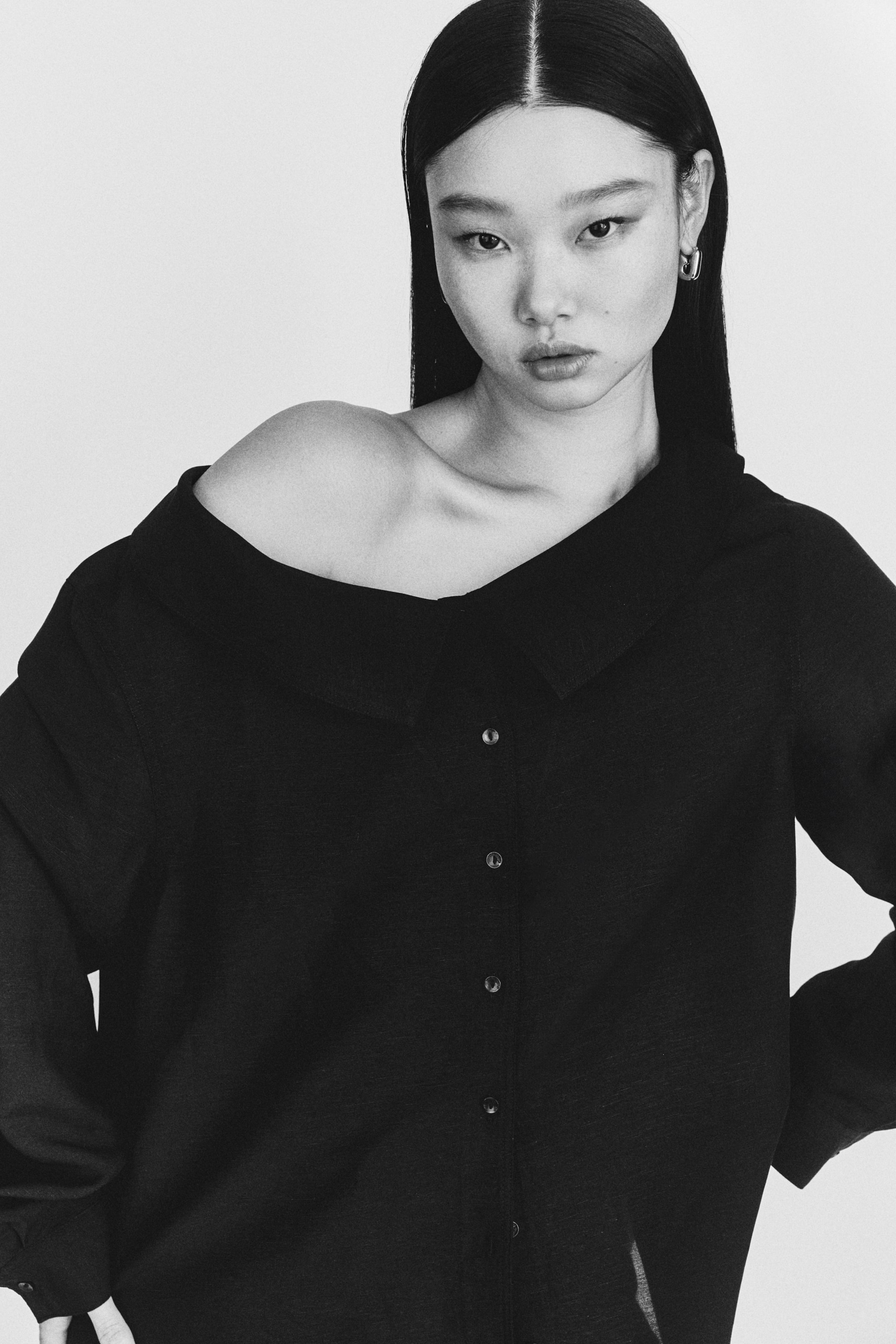 View larger image: A black button-front shirt is showcased with a spread collar styled off one shoulder. Long sleeves extend from its relaxed-fit body, with several dark buttons running down the front.