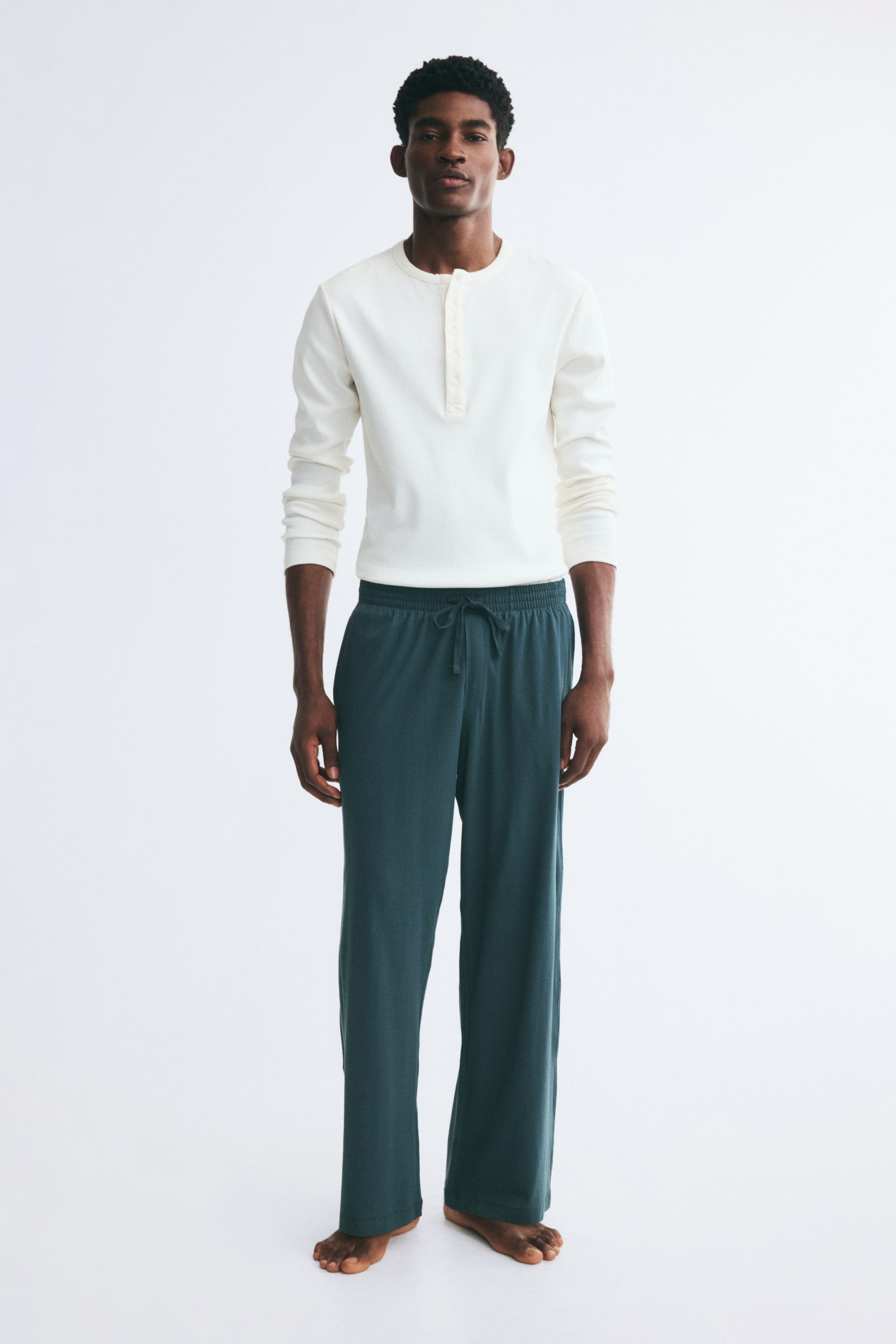 View larger image: Track pants in dark teal cotton jersey are worn by the model, featuring a straight-leg cut and an elasticated waistband with a tie drawstring. The regular-fit trousers are styled with a tucked-in, long-sleeved white henley shirt.
