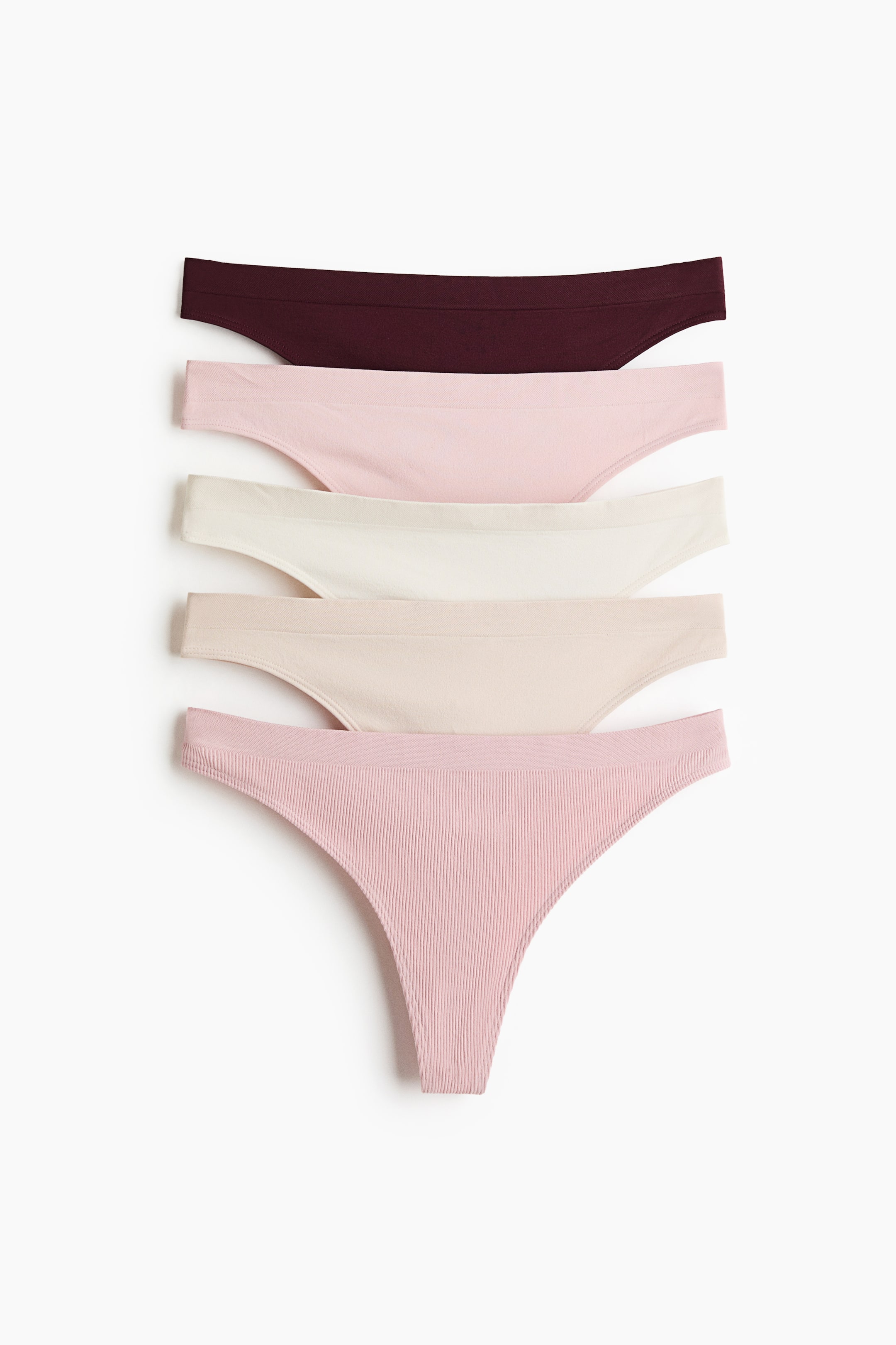 View larger image: Five thong briefs are showcased from the front, neatly stacked and fanned out. They boast a seamless design crafted from jersey material, presented in shades of maroon, light pink, cream, and light beige. The bottom brief highlights a ribbed texture in light pink.
