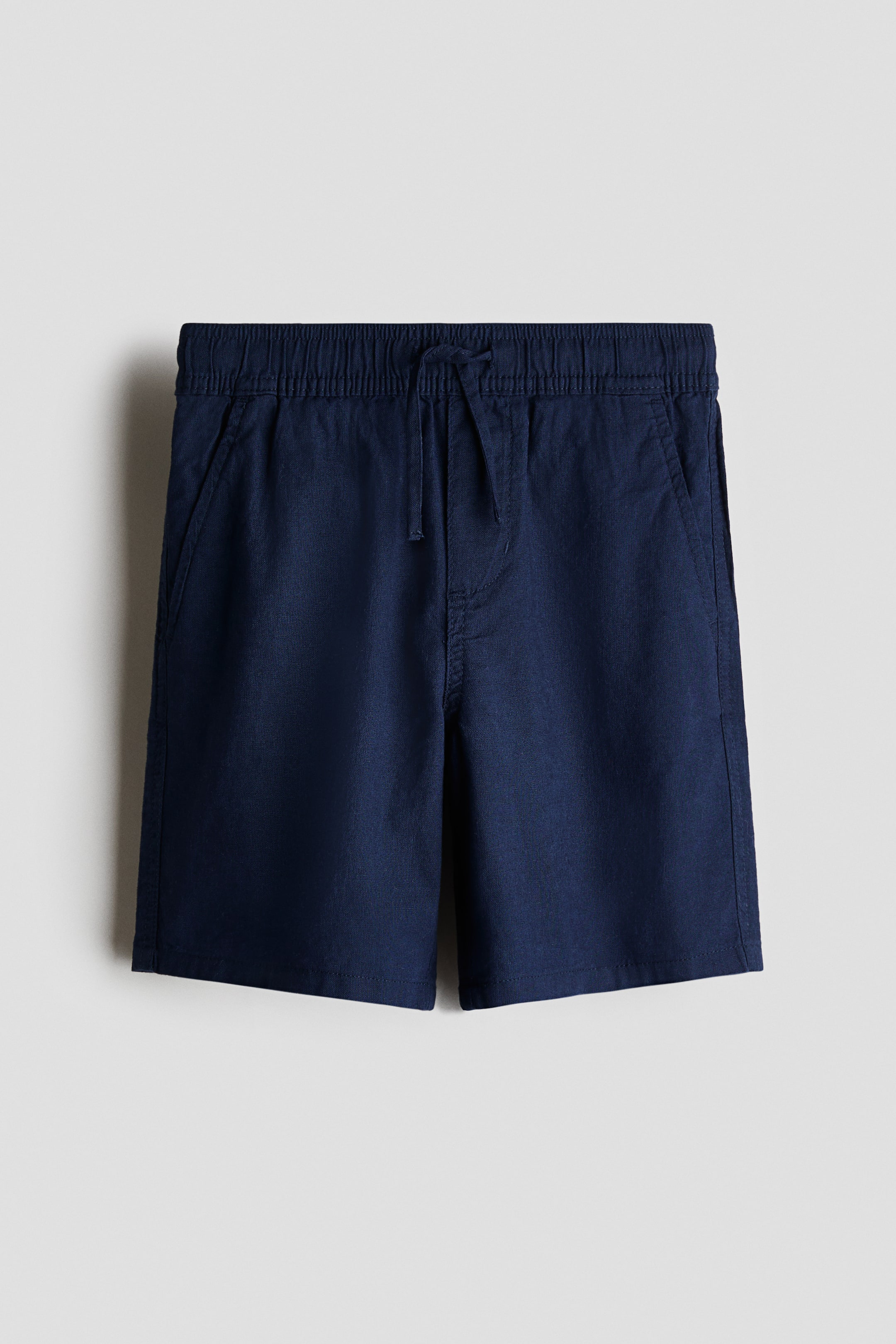 Ver imagen más grande: Pantalones cortos azul oscuro de cara frontal en tejido de algodón y lino, diseñados con cintura elástica con cordón, falsa bragueta y bolsillos frontales diagonales.