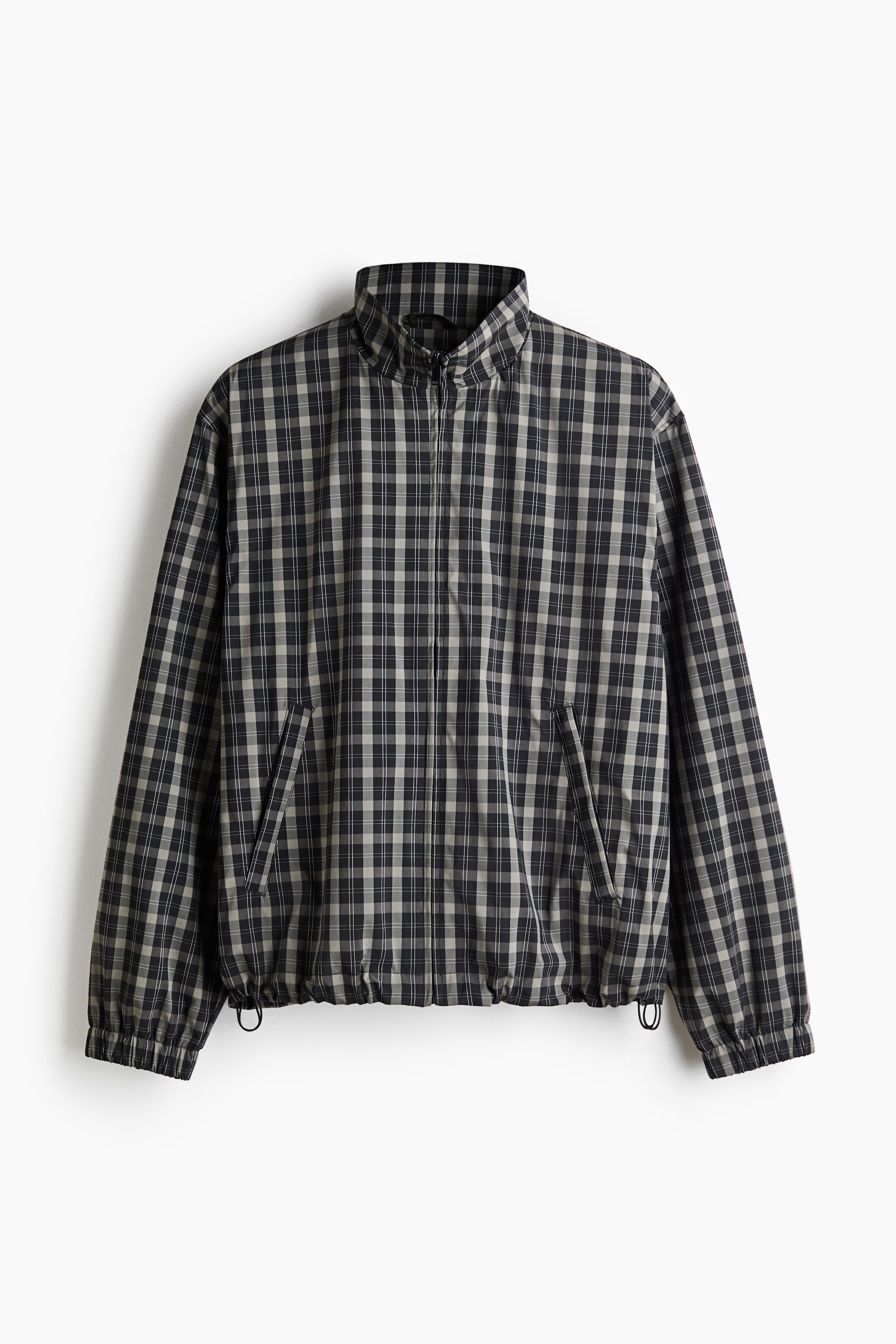 View larger image: The jacket showcases a black and beige plaid pattern on the front. It features a stand-up collar, a full-zip closure, two angled side pockets, and gathered elastic at the bottom hem and cuffs.