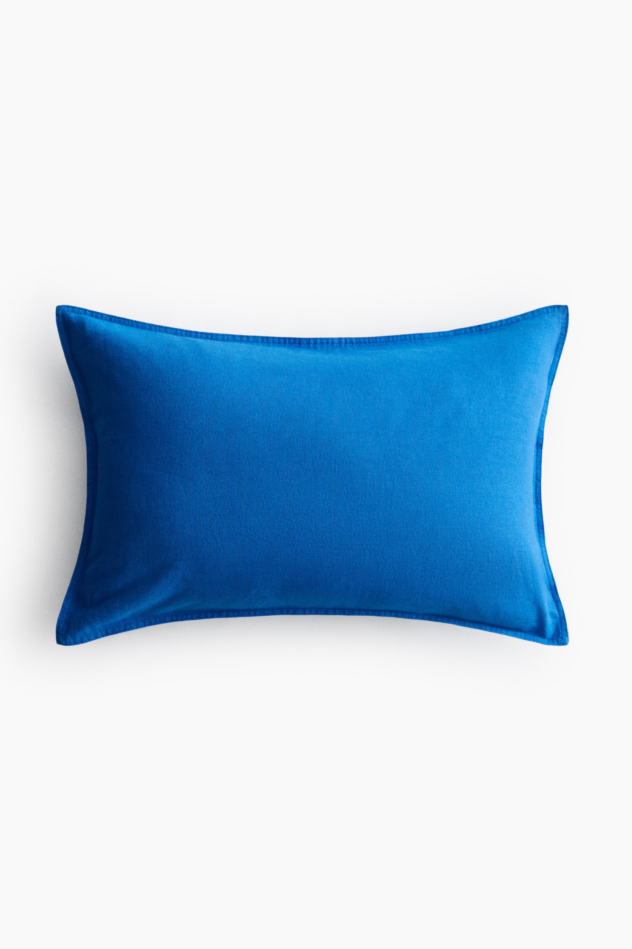 View larger image: A rectangular cushion cover is shown facing front, featuring a solid blue colour with a subtle woven texture. It displays prominent stitching along all four edges.