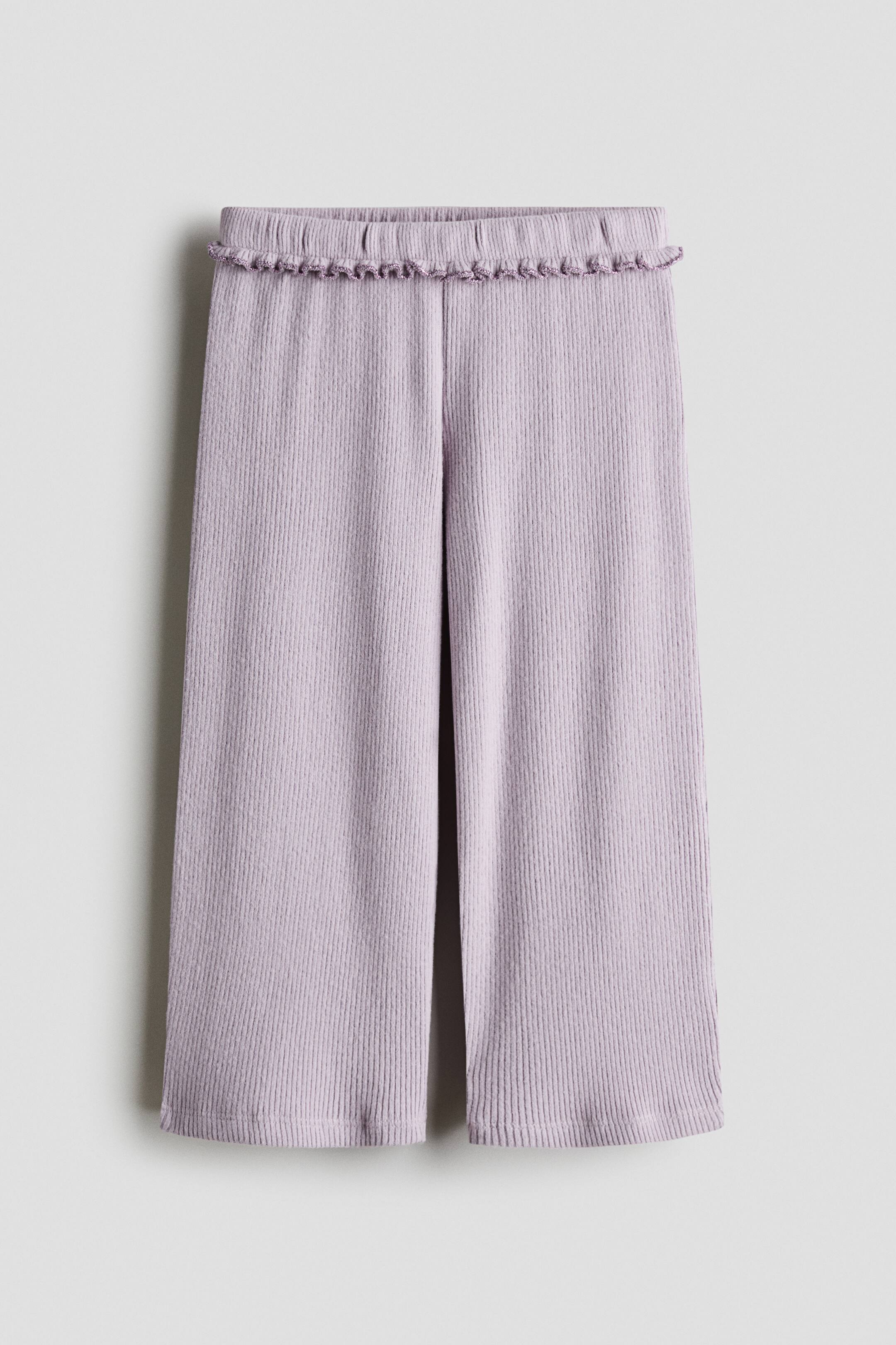 View larger image: Light purple wide-leg pants are shown from the front, featuring a vertical ribbed texture and an elasticized waistband adorned with a small ruffle trim. The pants fall straight down, showcasing a relaxed fit and wide legs.