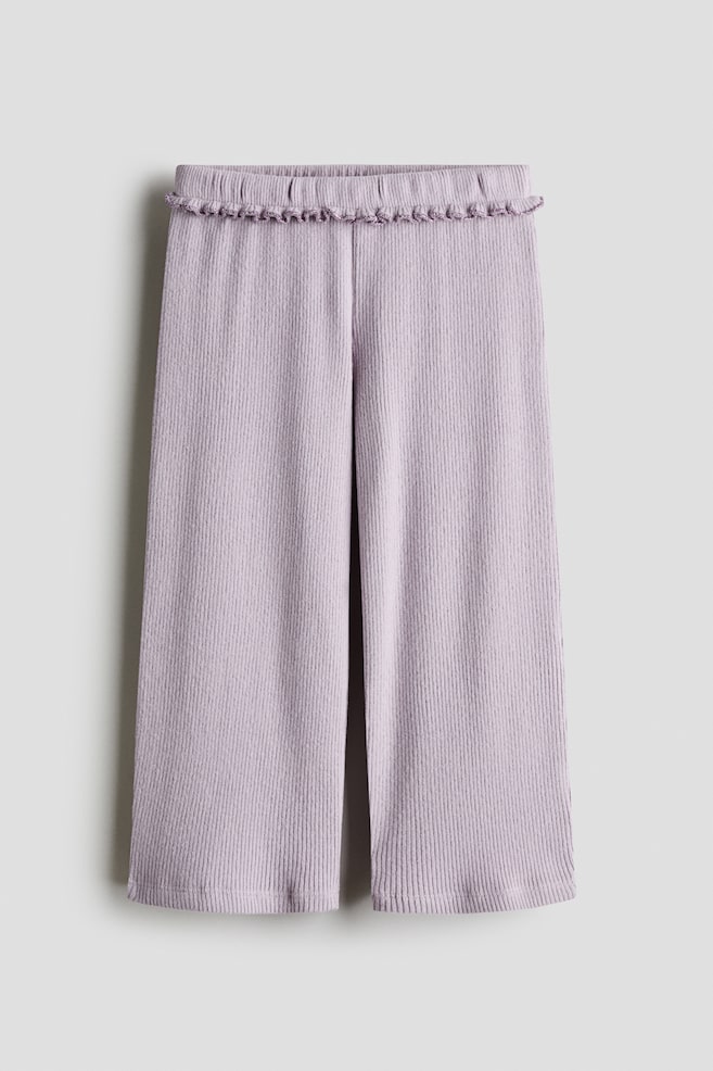 Light purple wide-leg pants are shown from the front, featuring a vertical ribbed texture and an elasticized waistband adorned with a small ruffle trim. The pants drape straight down, showcasing a relaxed fit and wide legs. - 1