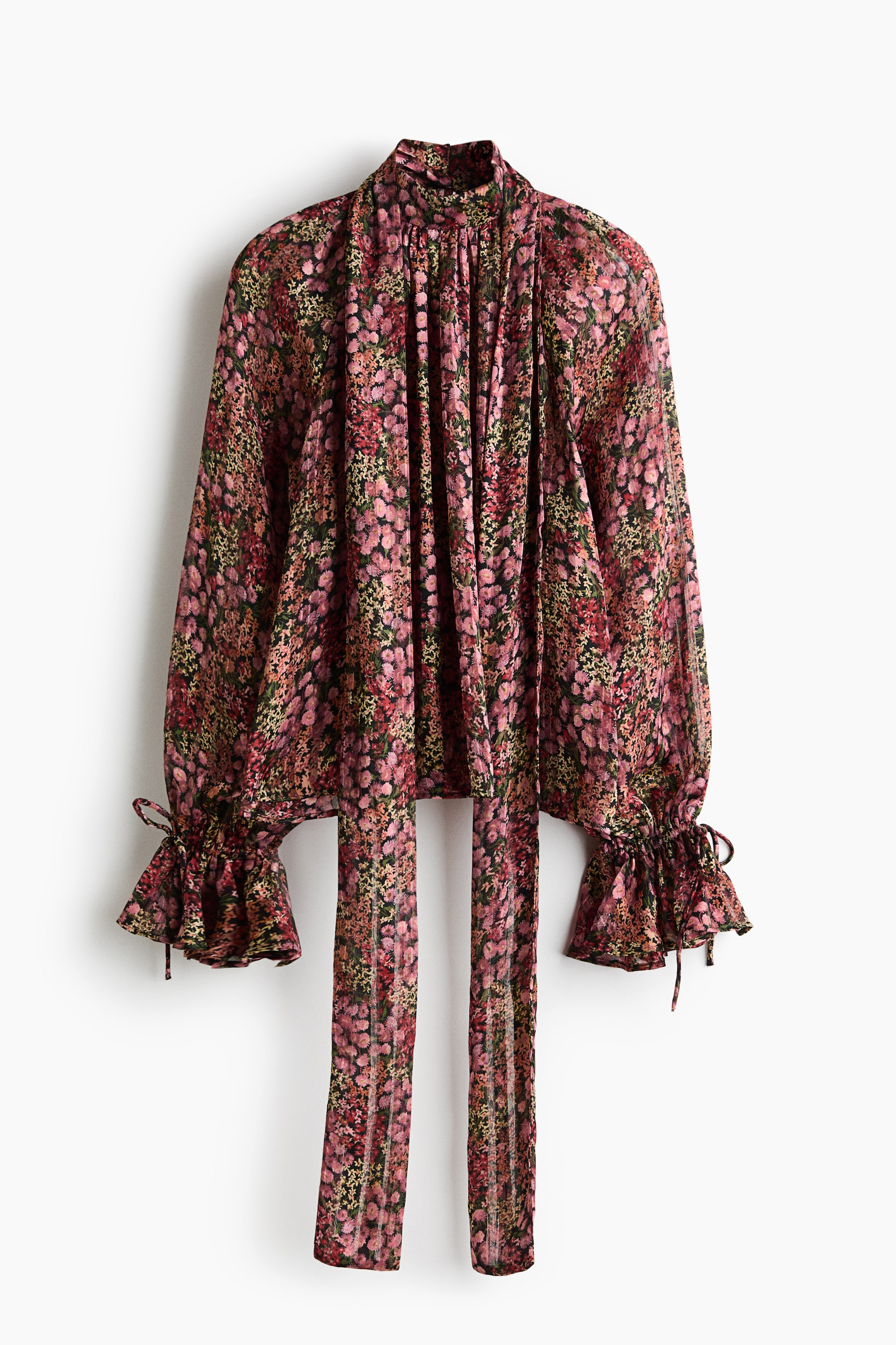 View larger image: A floral print blouse features a high, gathered neckline with two long fabric ties hanging down the front. It also features long, voluminous sleeves ending in ruffled cuffs with visible tie details.