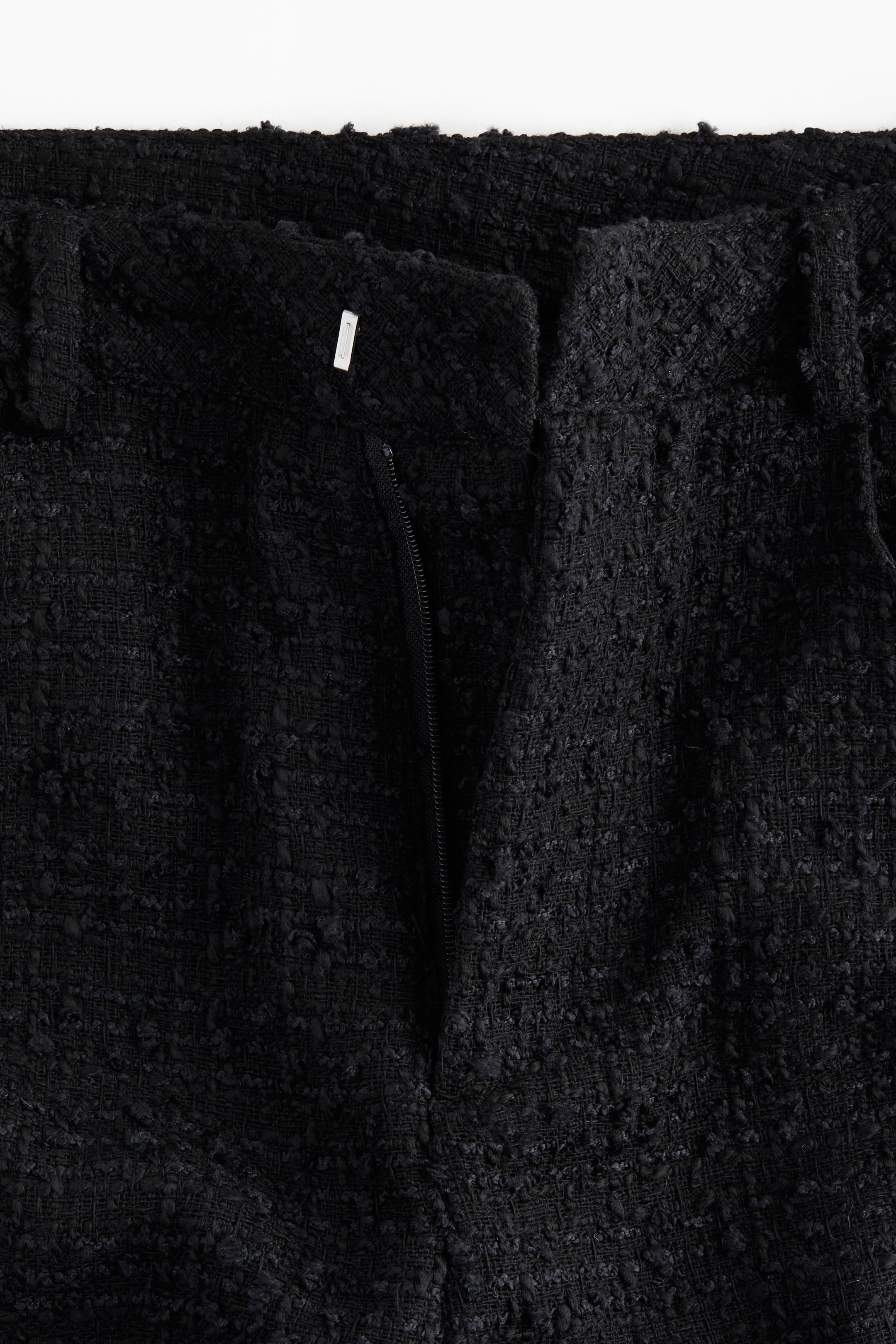 View larger image: A pair of black trousers is shown from a front view, featuring a textured bouclé-like fabric. The front zipper fly is partially open, and a metal hook-and-bar closure is visible at the waistband, which also includes belt loops.