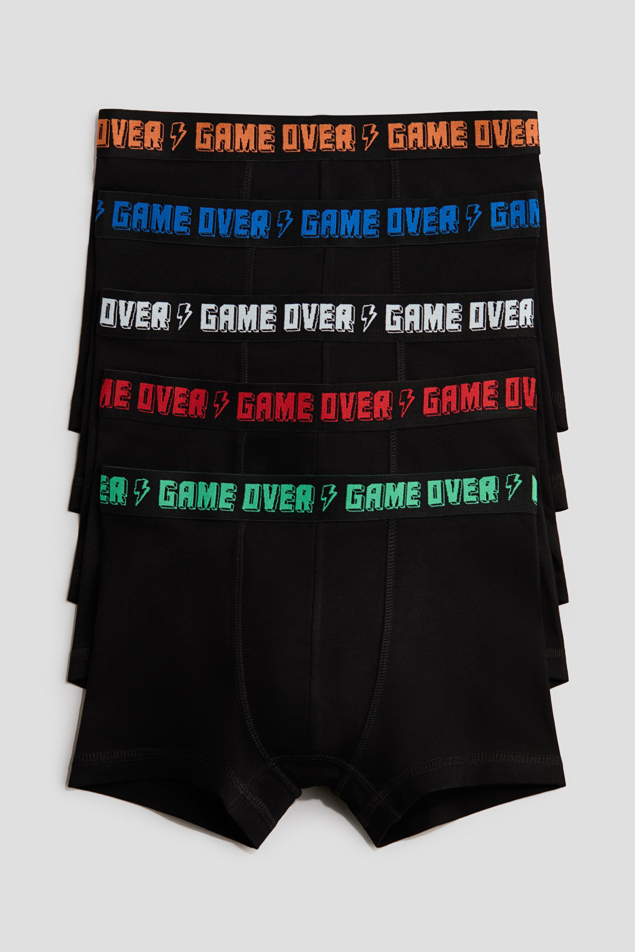 Zobacz większy obraz: Pięć czarnych bokserek z bawełnianej dzianiny (cotton jersey) ułożono w stos, prezentując PRZÓD. Każda bokserka ma krótkie nogawki, przód z podszewką oraz elastyczny pas z napisem "GAME OVER" i symbolem błyskawicy w kolorze pomarańczowym, niebieskim, białym, czerwonym lub zielonym.