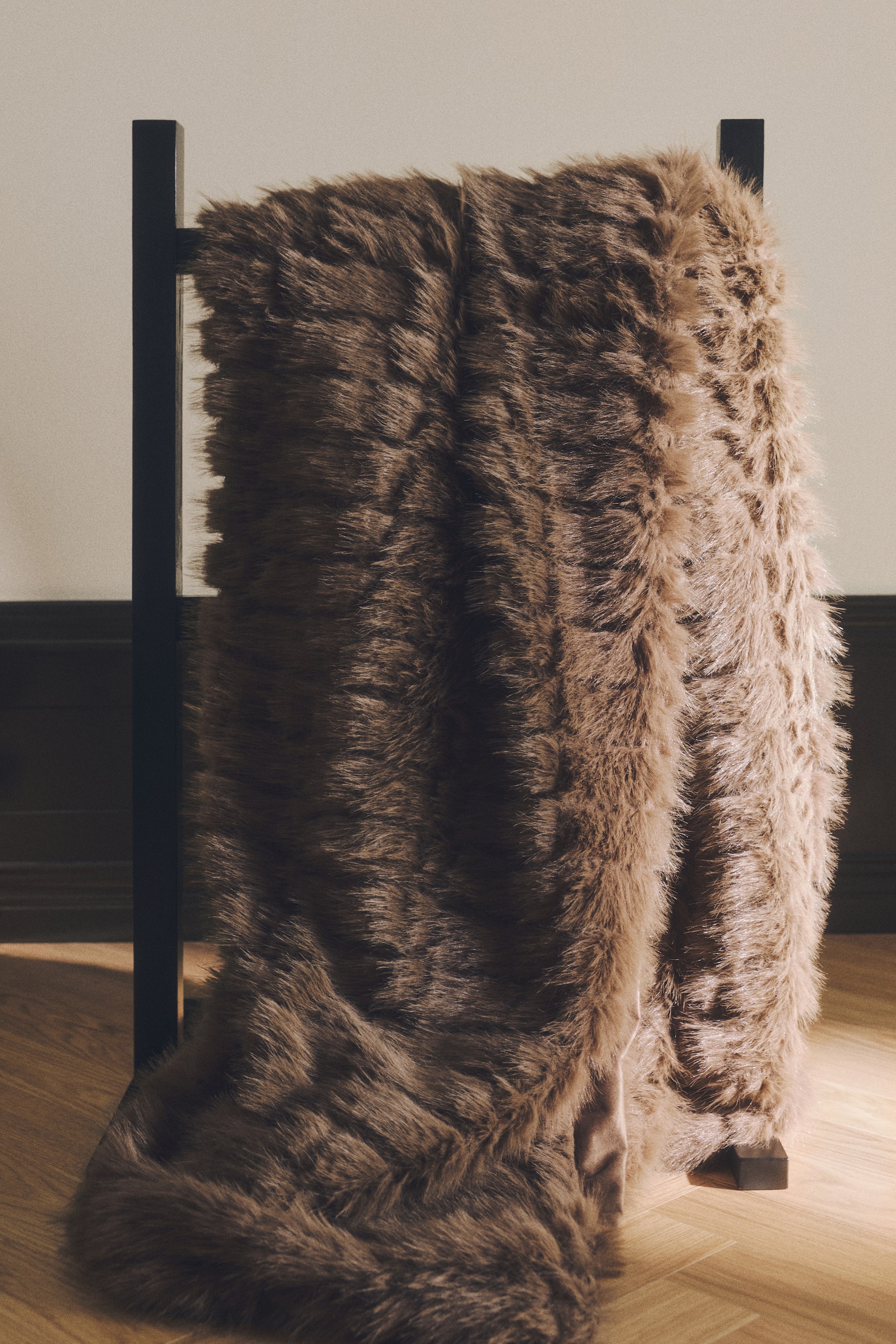 View larger image: A brown bed throw in a fluffy, long-pile faux-fur fabric is draping over a black wooden rack, showing its textured grid pattern on the front. The throw is pooling at the base, emphasising its soft, voluminous structure and revealing a glimpse of its smooth reverse lining.