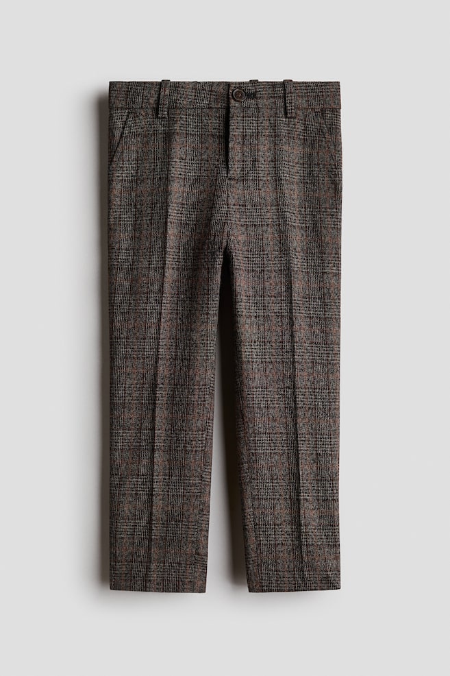 A front view showing slim-fit suit trousers in a brown and grey plaid cotton weave, featuring a button closure at the waistband, side pockets, and sharp creases running down the centre of each leg. - 1