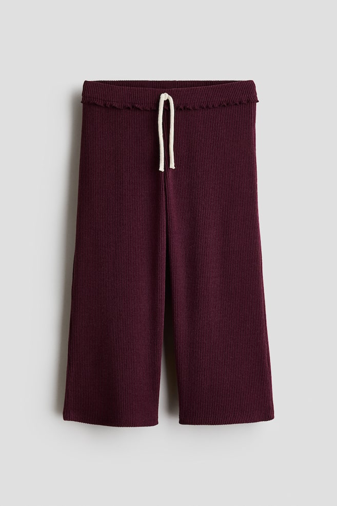 These wide-leg pants in a dark burgundy ribbed knit are shown facing front, featuring an elasticated waistband with a frill-trimmed edge and a decorative cream-colored drawstring at the center. - 1