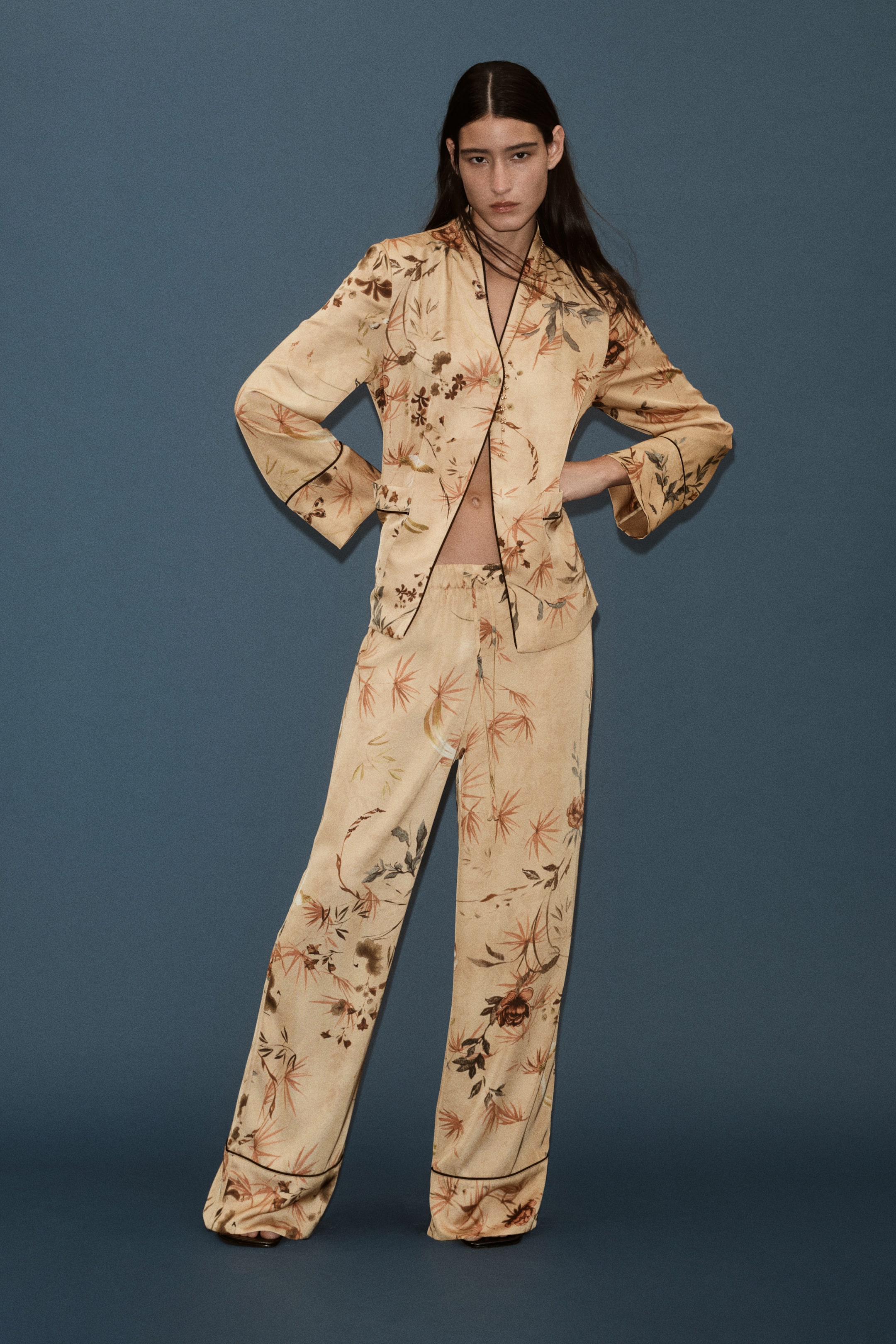 Ampliar la imagen: La modelo lleva puestos pantalones de tejido estampado con un estampado botánico, cintura elástica con cordón ajustable y piernas rectas con bajos rematados con vivo. Los pantalones se combinan con una camisa de manga larga a juego con estampado botánico.