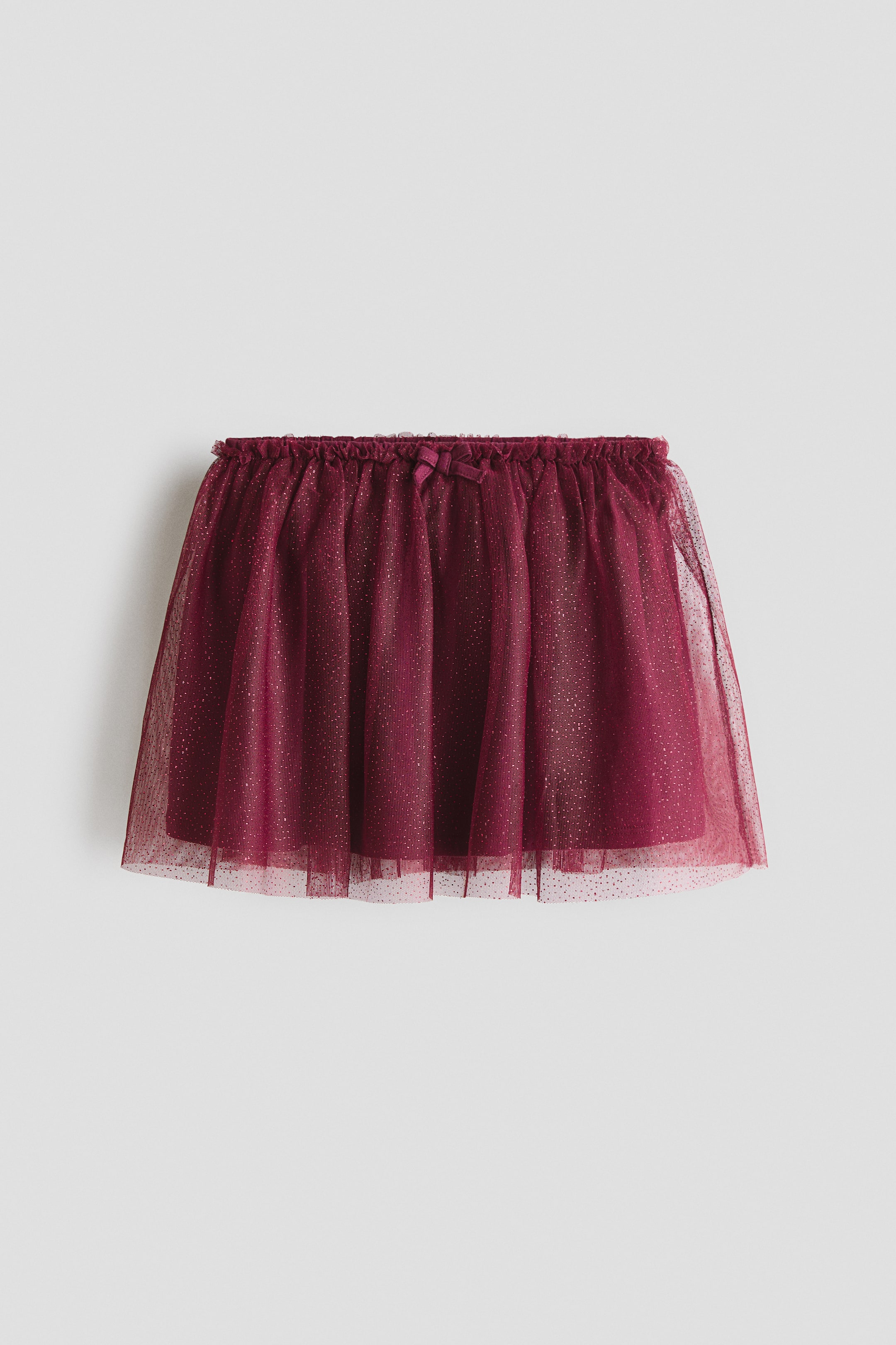 Ver imagen más grande: Se presenta una falda de malla con brillo color burdeos en vista frontal, con múltiples capas de tul fruncido que crean una silueta amplia. Está diseñada con cintura elástica y un pequeño lazo decorativo en la parte delantera.