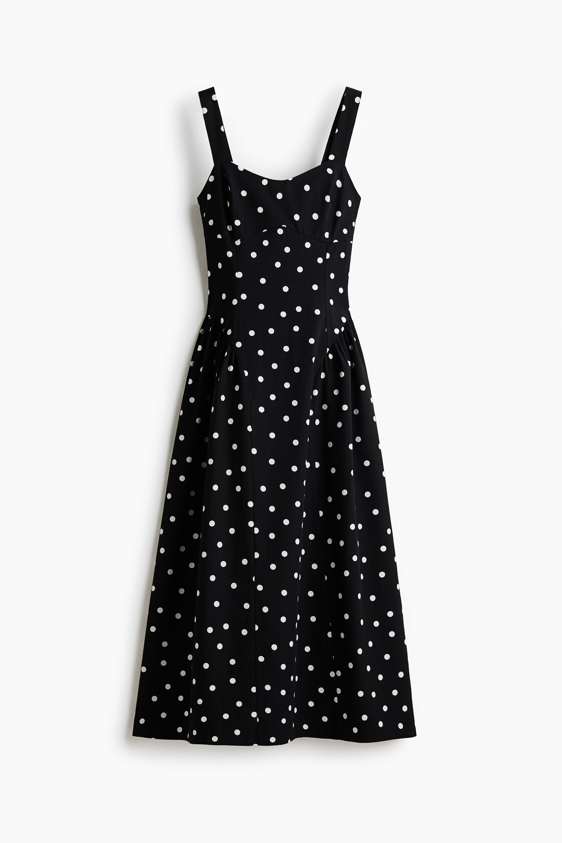Ein schwarzes, knÃ¶chellanges Kleid mit weiÃem Polka-Dot-Muster wird von dem Model getragen, das mit verschrÃ¤nkten Armen steht. Das Kleid verfÃ¼gt Ã¼ber einen Herzausschnitt mit breiten TrÃ¤gern, ein tailliertes Oberteil und einen ausgestellten Rock mit gerafften NÃ¤hten Ã¼ber den HÃ¼ften.
