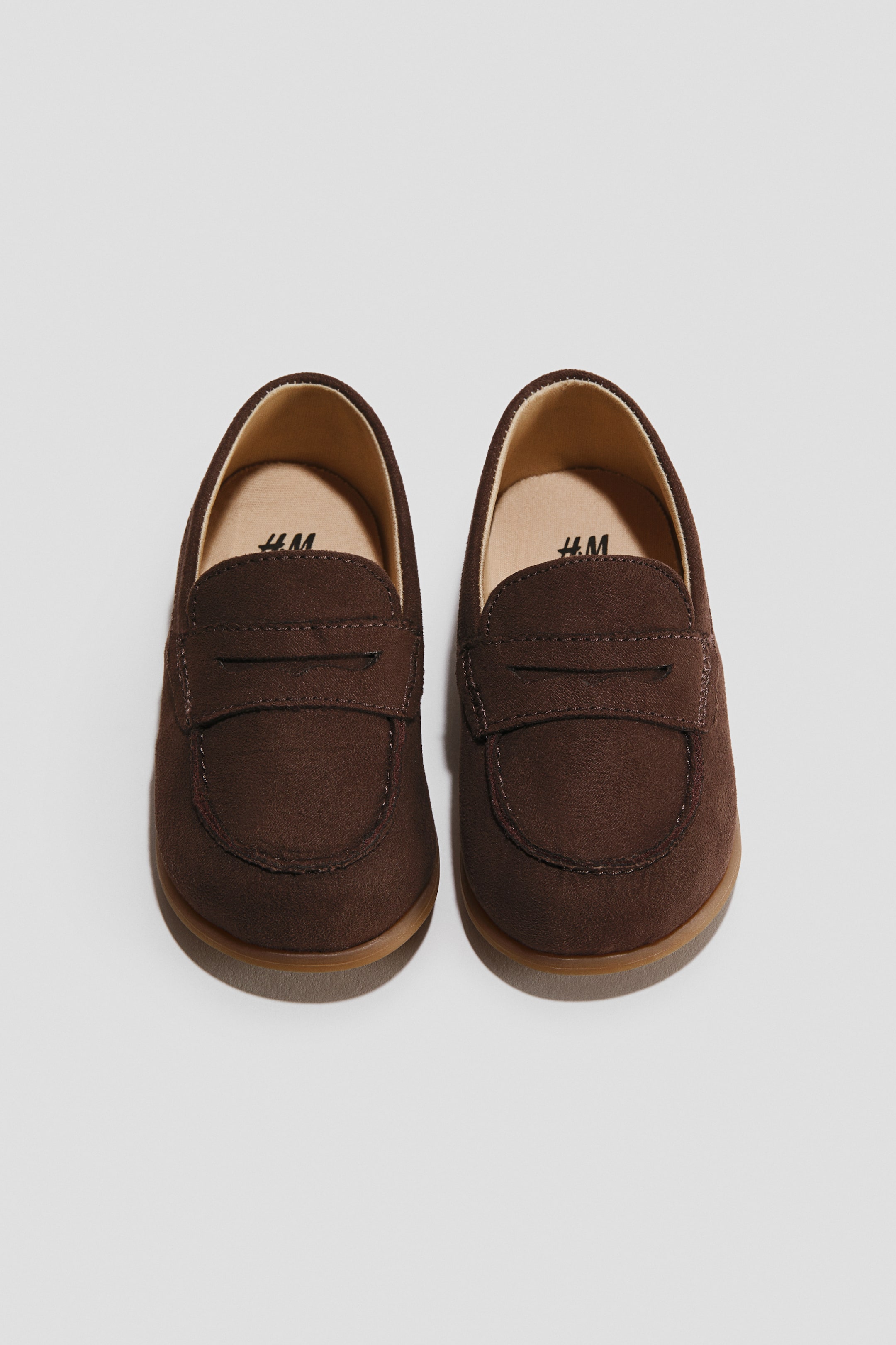 View larger image: These dark brown barefoot loafers are facing forward, showcasing a soft faux-suede upper with a classic penny strap and stitched moc-toe detailing. The shoes feature a wide, rounded toe box, beige insoles, and thin, flat gum outsoles.