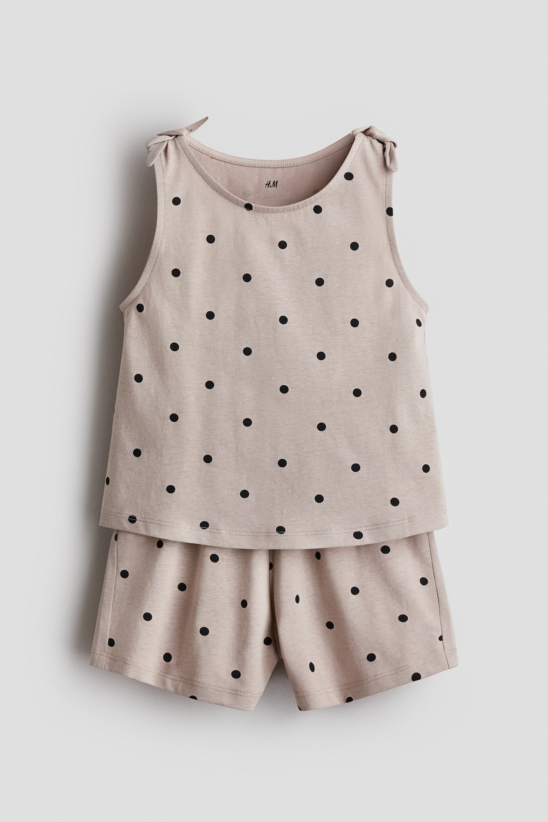 Visualizza l'immagine ingrandita: Un set pigiama a due pezzi presenta un top senza maniche beige e pantaloncini coordinati, entrambi decorati con pois neri. Il top presenta uno scollo rotondo e dettagli con lacci che formano fiocchi su entrambe le spalle.
