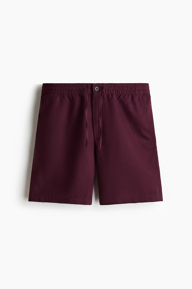 Los shorts color burdeos presentan un ajuste regular y una tela texturizada, vistos desde el frente. Cuentan con una pretina elástica cubierta con cordón y cierre de botón, junto con bolsillos visibles en la costura lateral. - 1