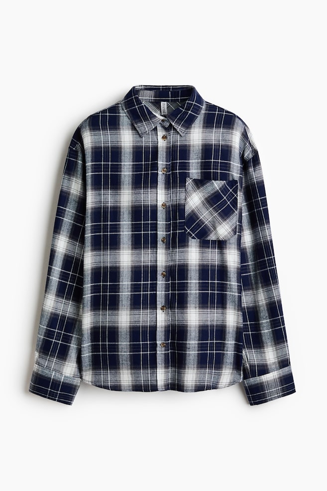 Koszula flanelowa z dÅugim rÄkawem w granatowo-biaÅÄ kratÄ jest ustawiona przodem, prezentujÄc koÅnierzyk typu point collar oraz peÅnÄ listwÄ guzikowÄ z brÄzowymi guzikami. Ma pojedynczÄ naszywanÄ kieszeÅ na piersi z ukoÅnie uÅoÅ¼onym wzorem w kratÄ oraz mankiety zapinane na guziki przy dÅugich rÄkawach. - 1