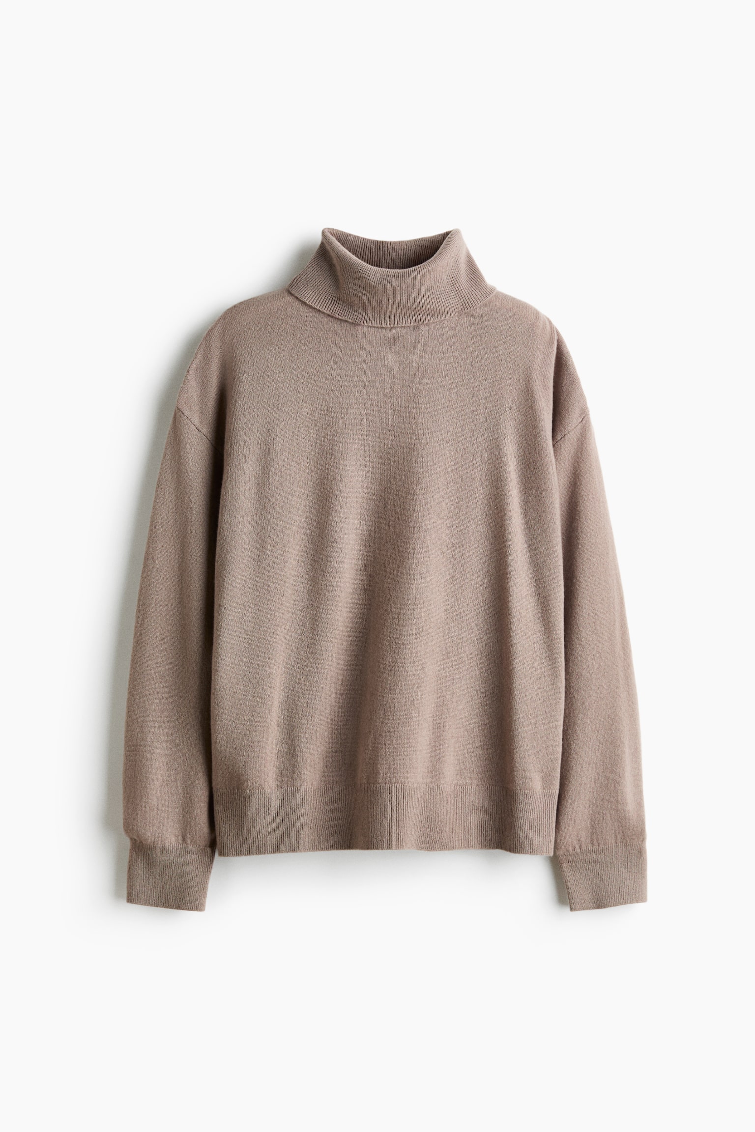 Een taupe fijngebreide kasjmier trui hangt plat en toont de voorkant, met een oversized silhouet, een geribde coltrui, verlaagde schouders en lange mouwen afgewerkt met geribde boorden en een geribde zoom.