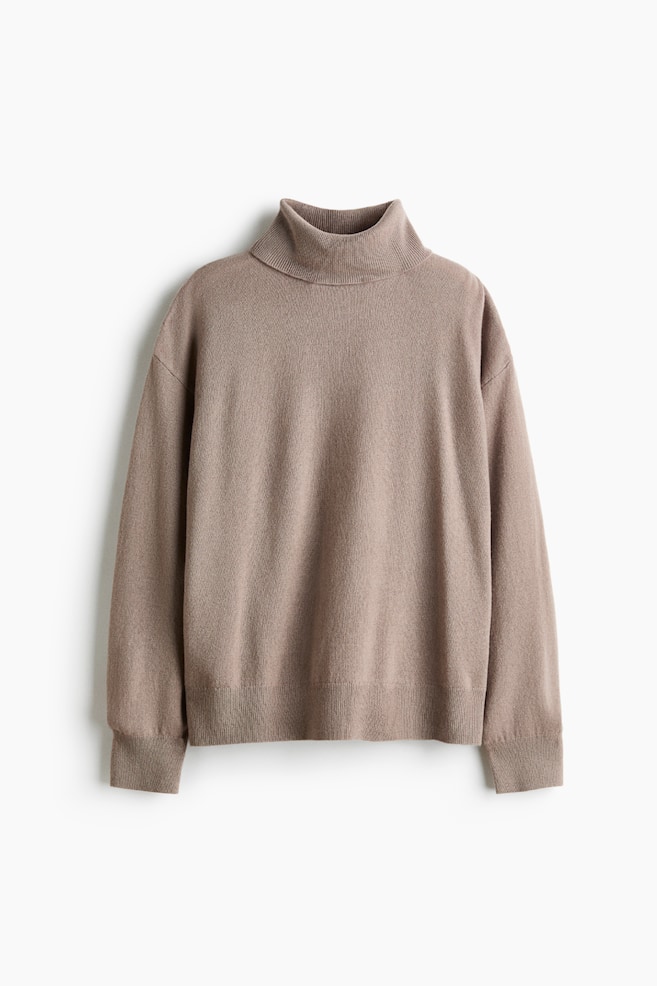 A taupe fine-knit cashmere jumper is hanging flat and facing the front, displaying an oversized silhouette with a ribbed roll neck, dropped shoulders, and long sleeves finished with ribbed cuffs and a ribbed hem. - 1